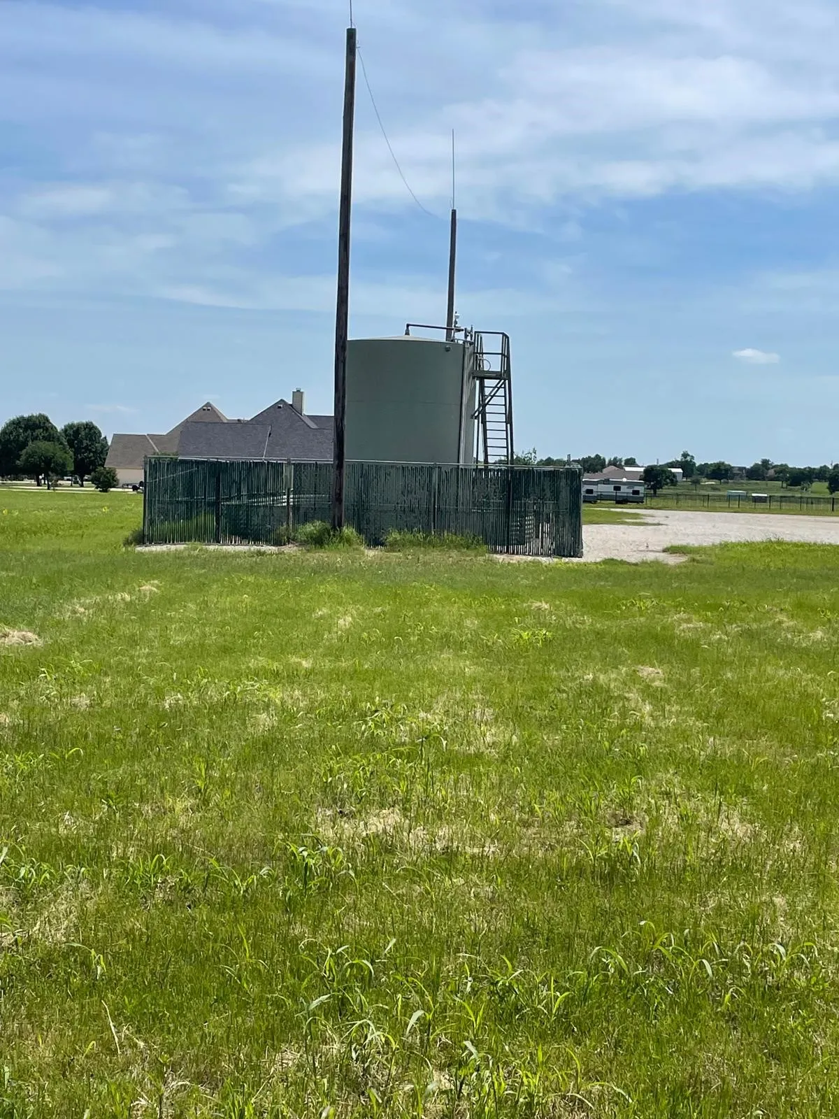 Fenced utility structure featuring a large cylindrical tank with an attached metal ladder