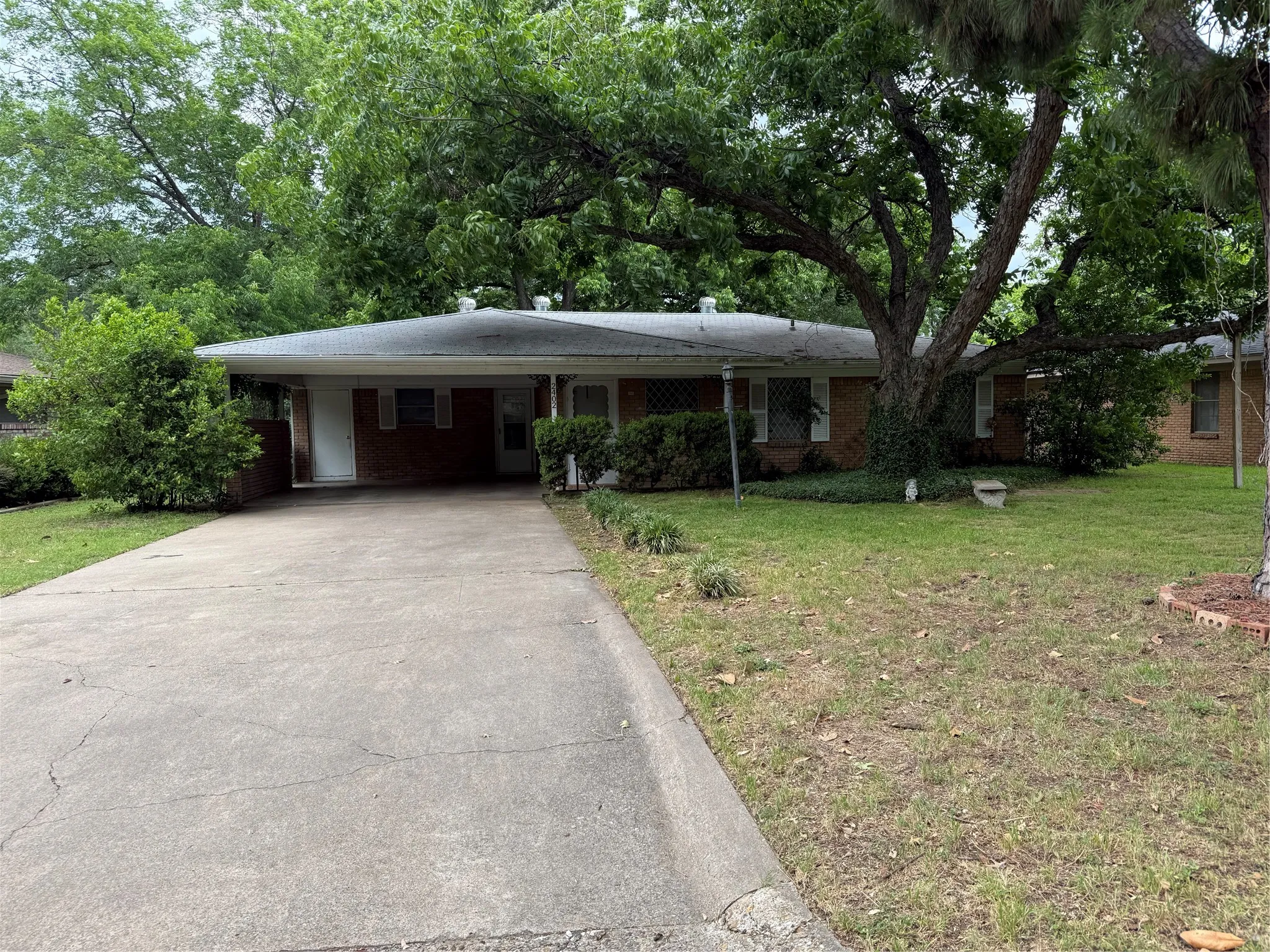Brick exterior home featuring a carport, concrete driveway, and mature landscaping