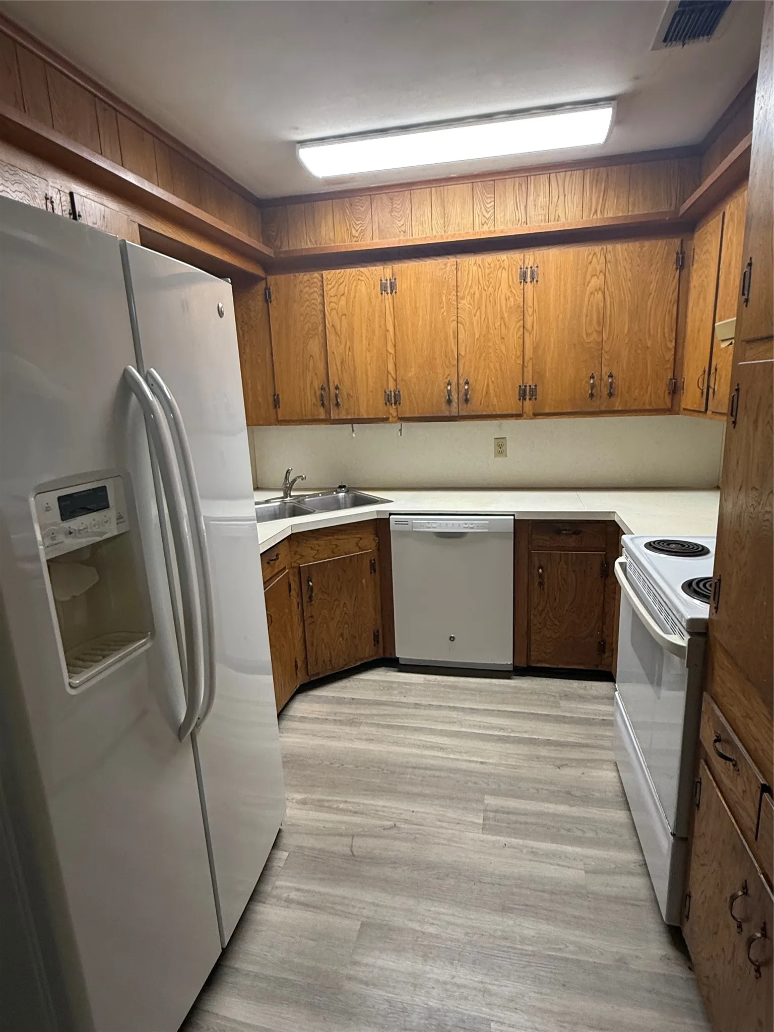 Kitchen featuring light wood-finish flooring, white countertops, extensive wood cabinetry, and a double basin sink