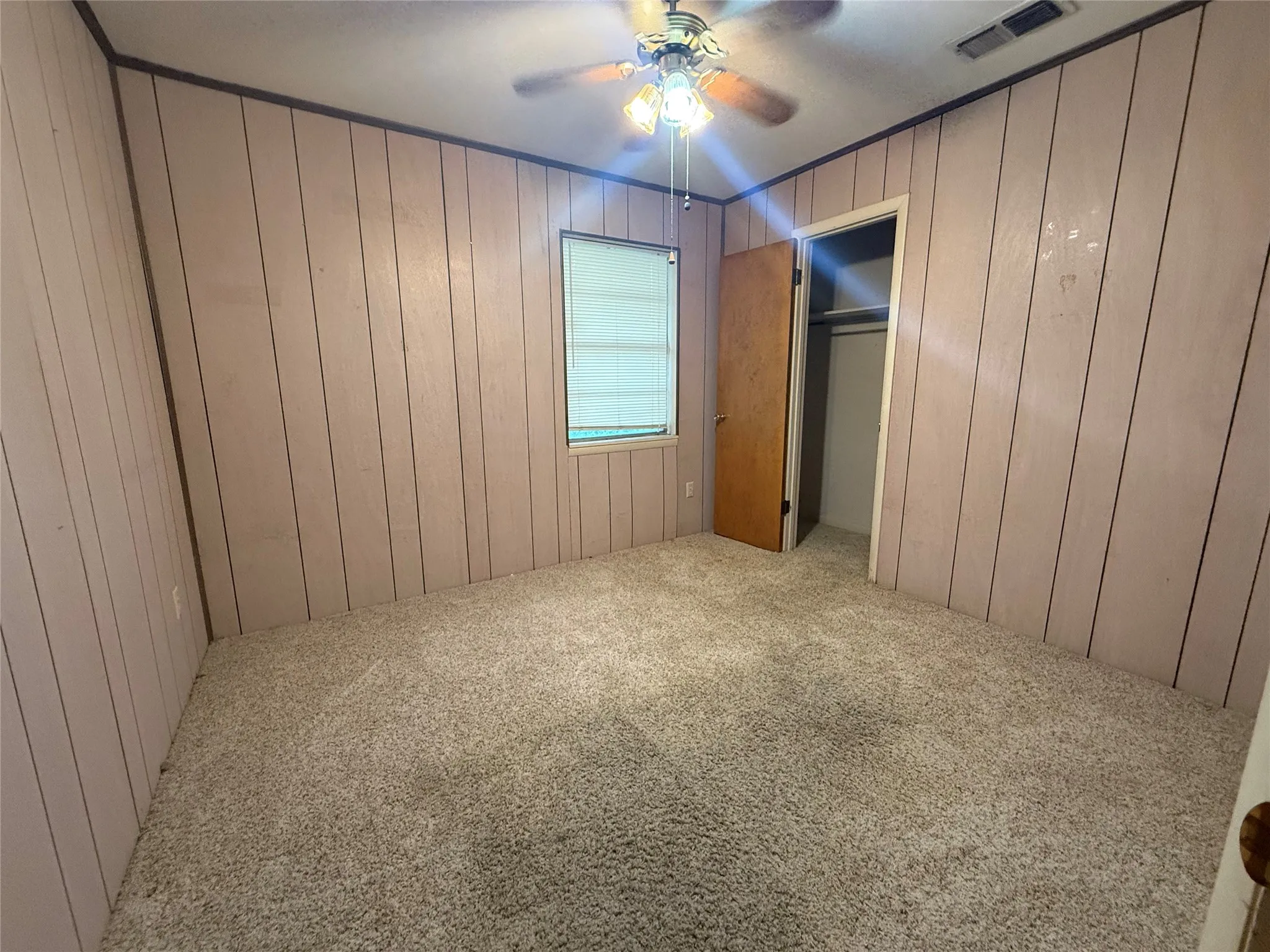 Carpeted room featuring vertical wood paneling, a window with blinds, and a ceiling fan with integrated lighting