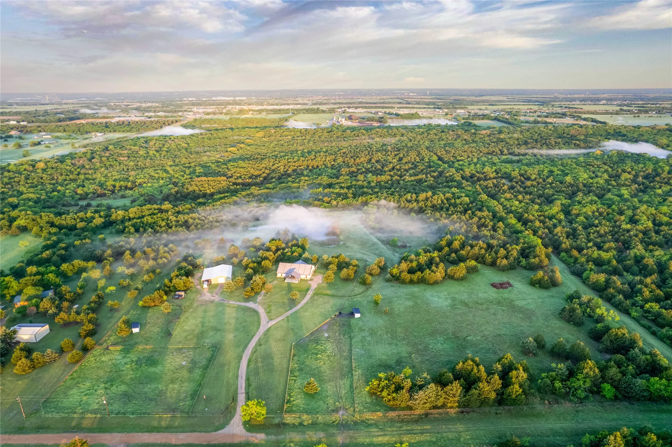 Expansive rural property featuring a primary residence, a secondary structure, and a winding driveway amidst extensive green space and mature trees