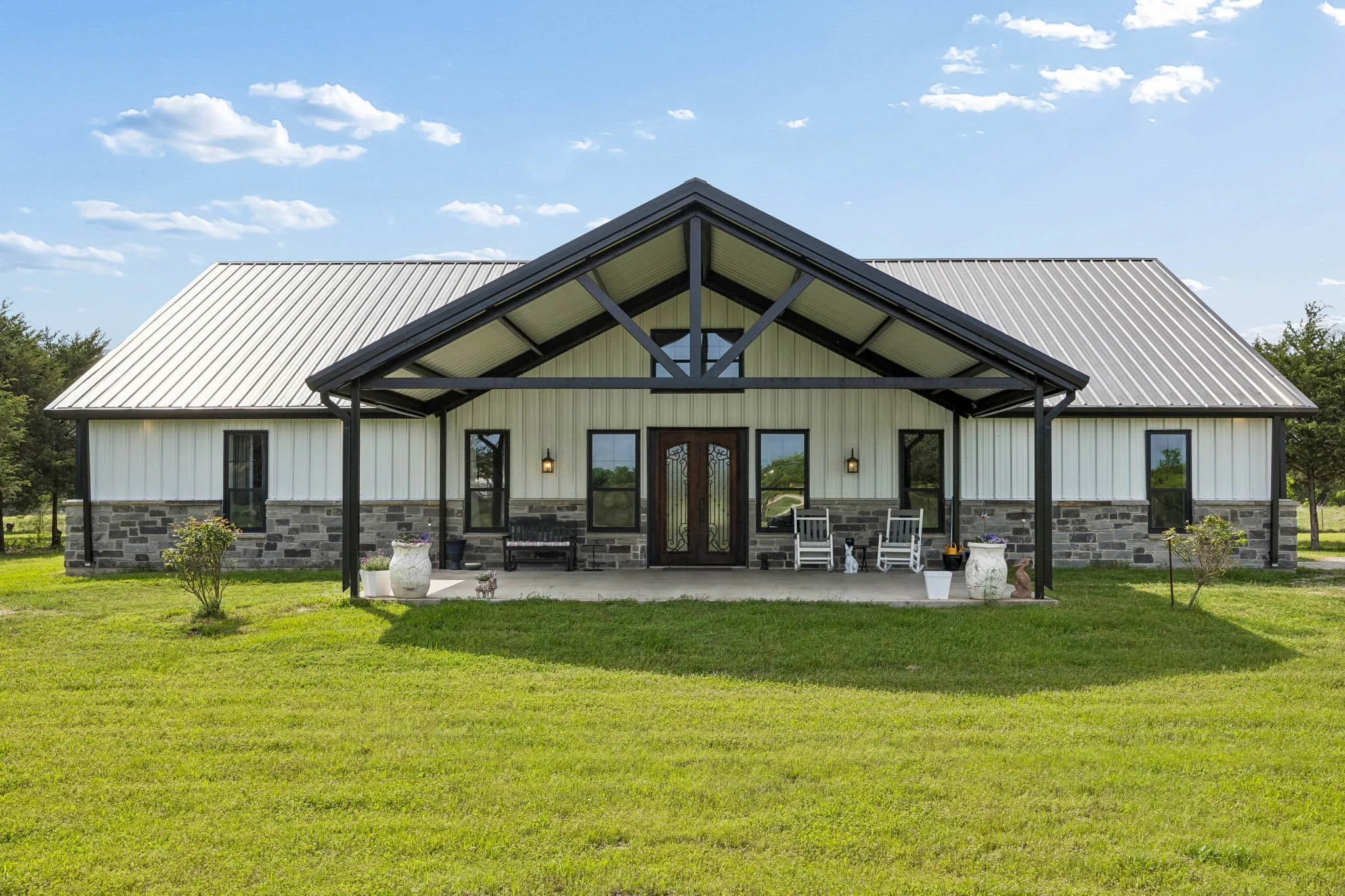 Modern farmhouse exterior featuring a prominent covered front porch, a metal roof, board and batten siding, stone wainscoting, and a double entry door with decorative glass