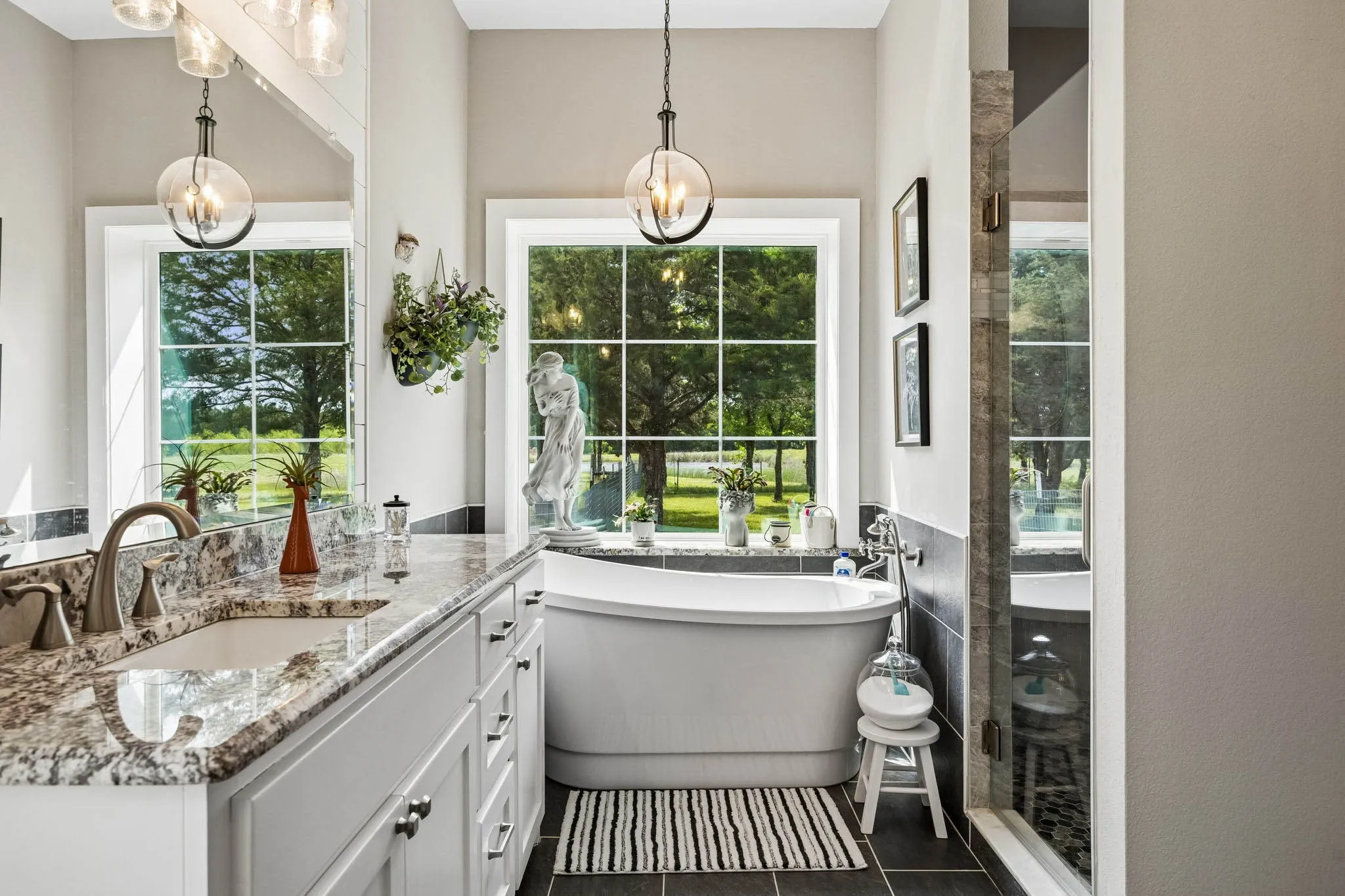 Bright bath featuring a freestanding soaking tub, dual-pane windows, a generously sized vanity with a built-in sink, stone countertop, and a glass-enclosed shower