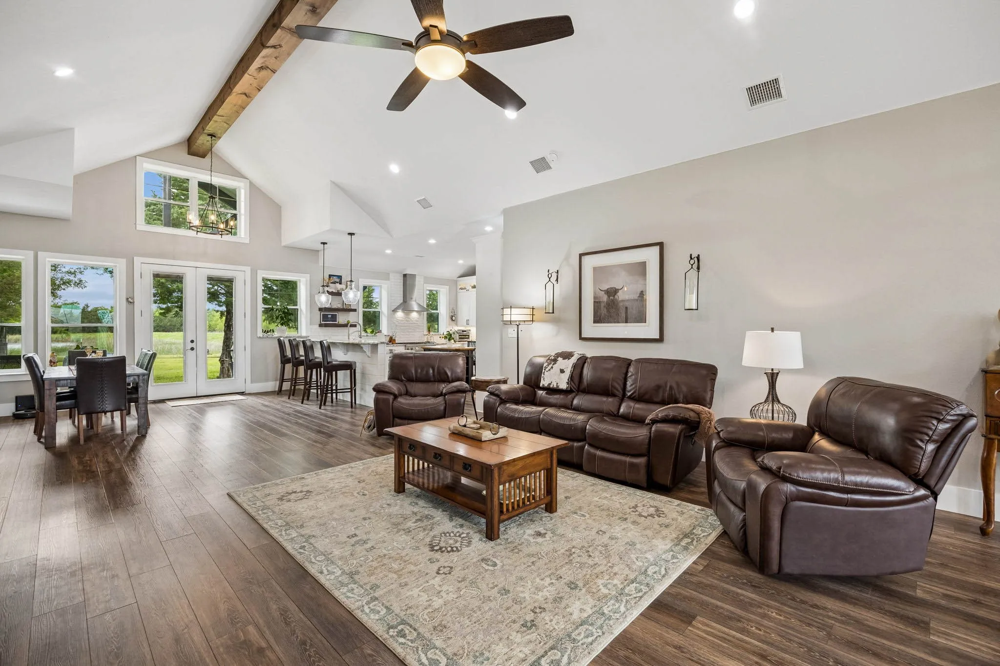 Spacious open-concept living area featuring high vaulted ceilings with a prominent exposed wood beam and a ceiling fan