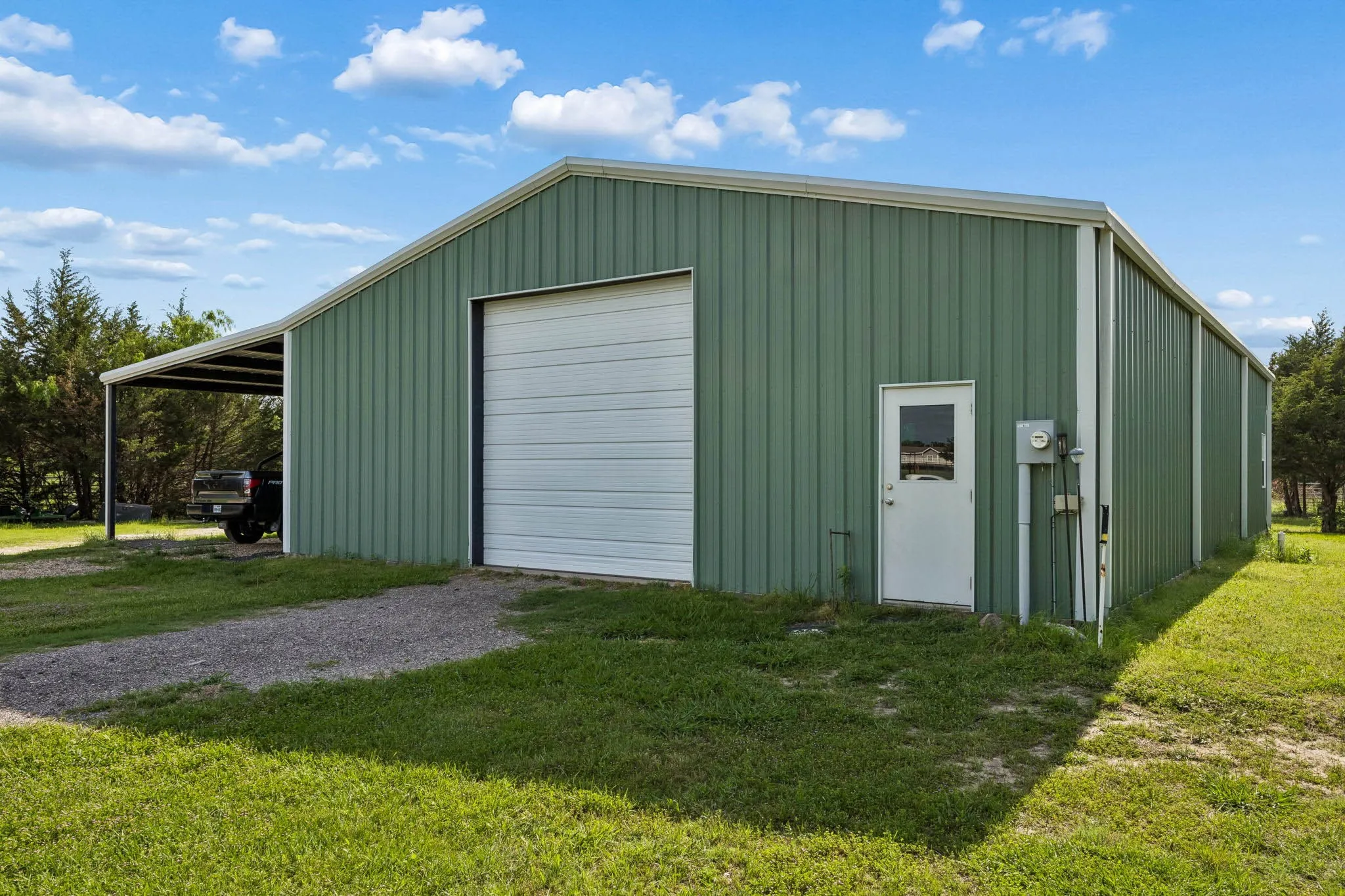 Metal-sided structure featuring a large roll-up garage door, an entry door with a window, and an attached covered carport