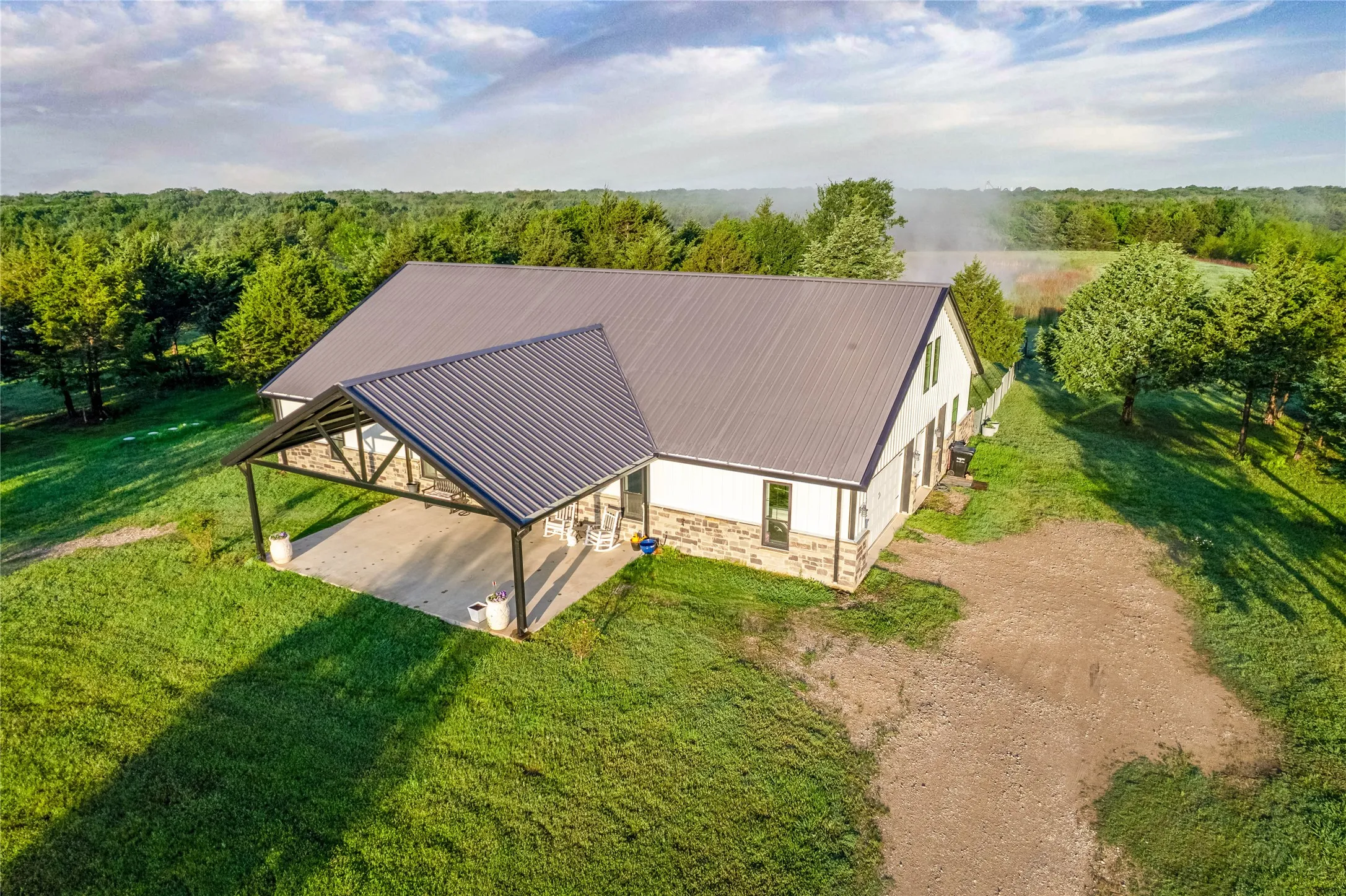 Single-story residence featuring a gray metal roof, white siding, and a stone veneer foundation