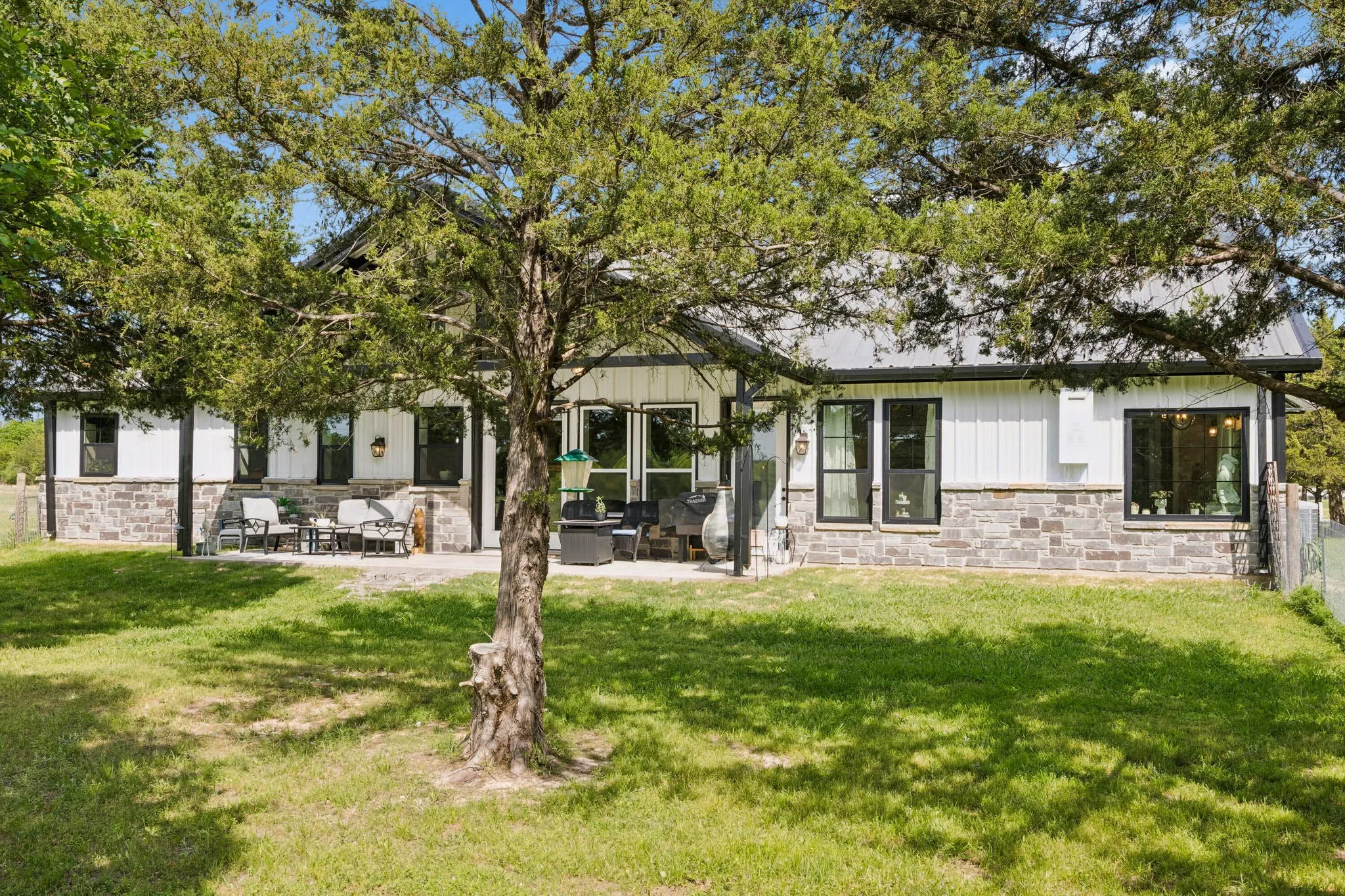 Rear elevation featuring a stone and board-and-batten facade, multiple large windows, a covered patio area, and a metal roof