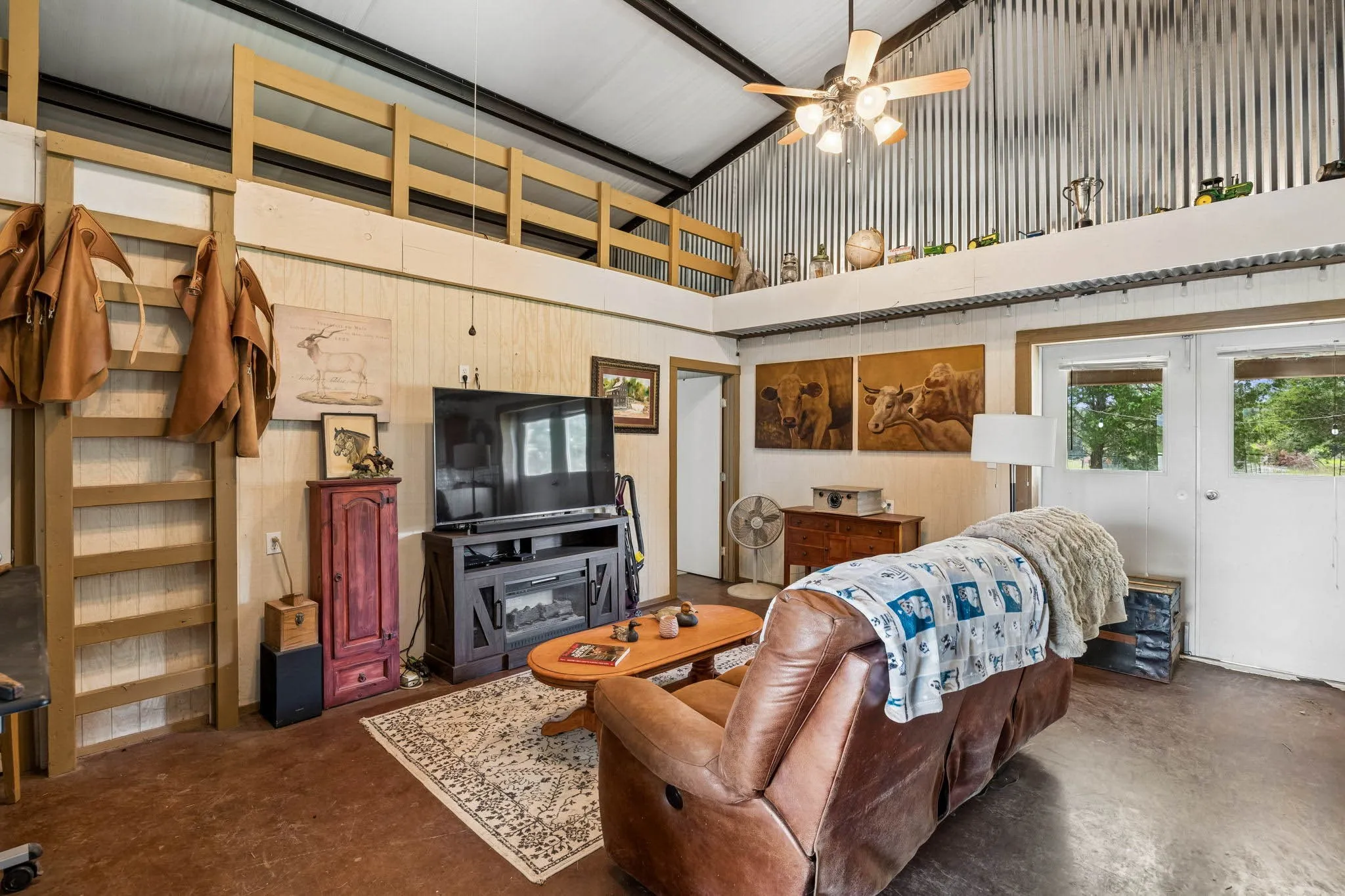 Living area featuring a high corrugated metal ceiling, exposed beams, a ceiling fan with integrated lighting, and a built-in media console with an electric fireplace