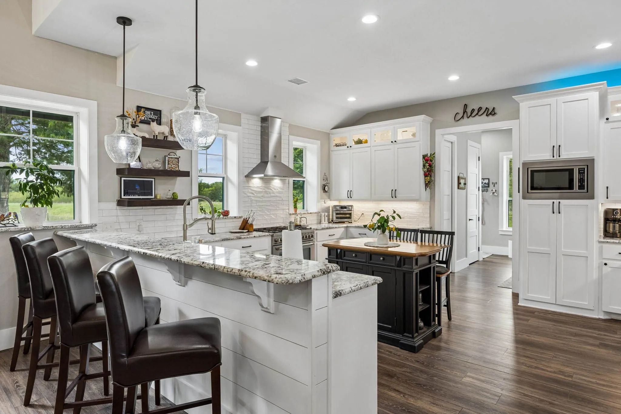Spacious kitchen featuring an extended island with granite countertops, integrated stainless-steel appliances, white shaker cabinetry, and wood-finish flooring