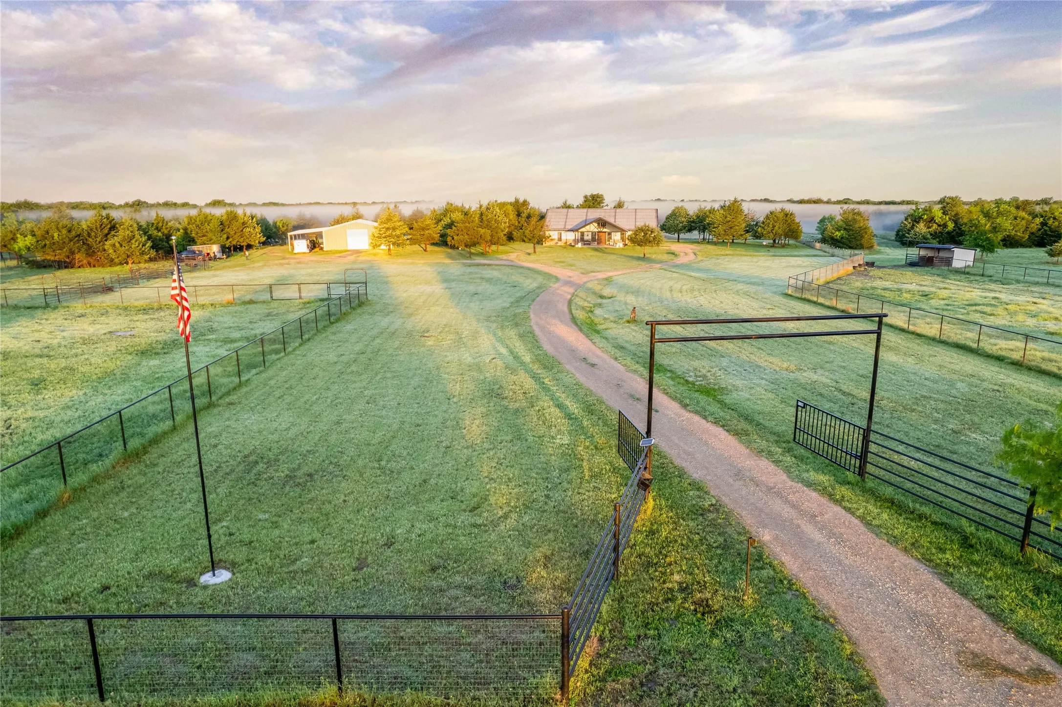 Expansive property featuring a winding gravel driveway, a large main residence, a secondary building, and perimeter fencing