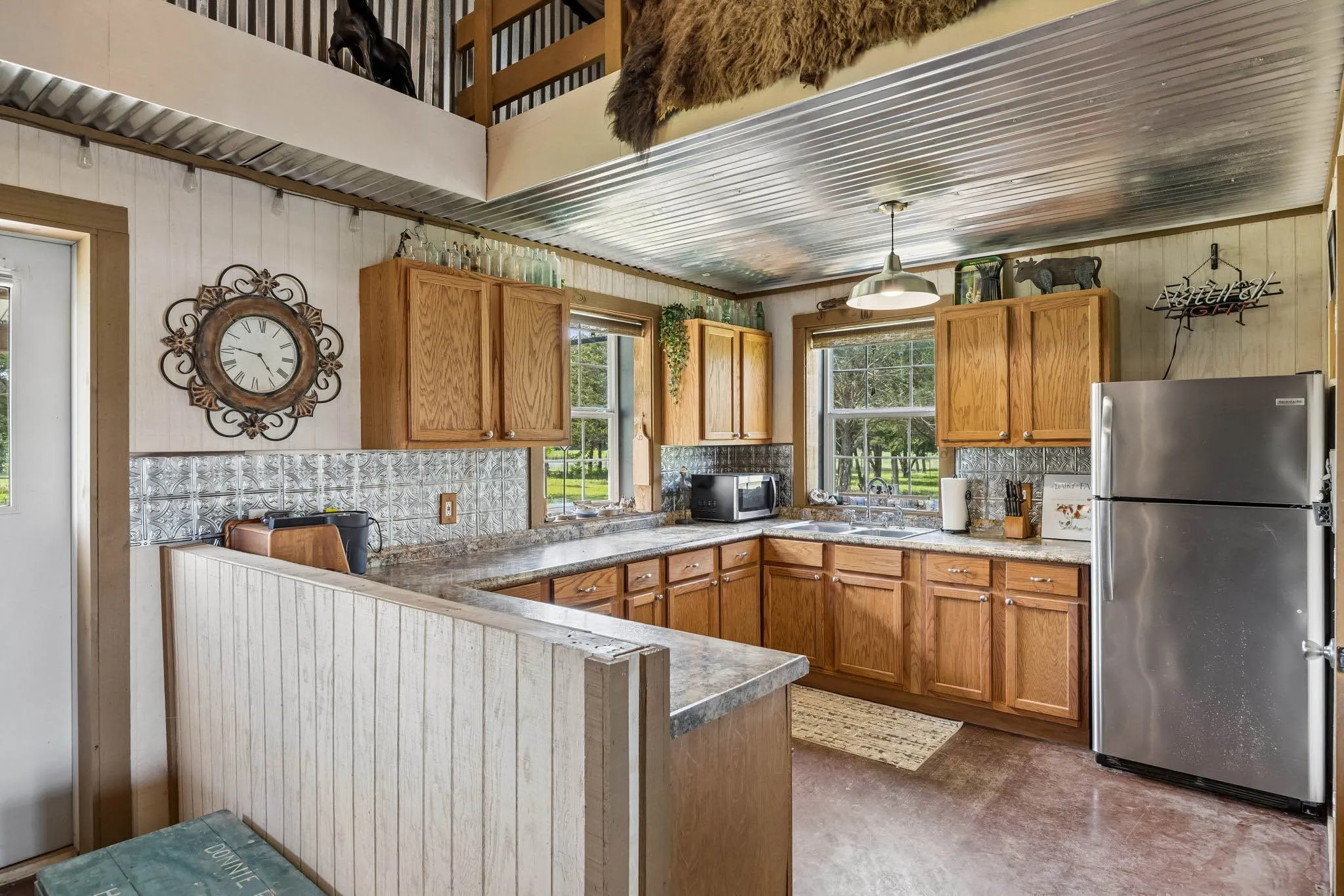Open-concept kitchen featuring wood-finish cabinetry, a metal corrugated ceiling, stainless steel appliances, and durable countertop surfaces