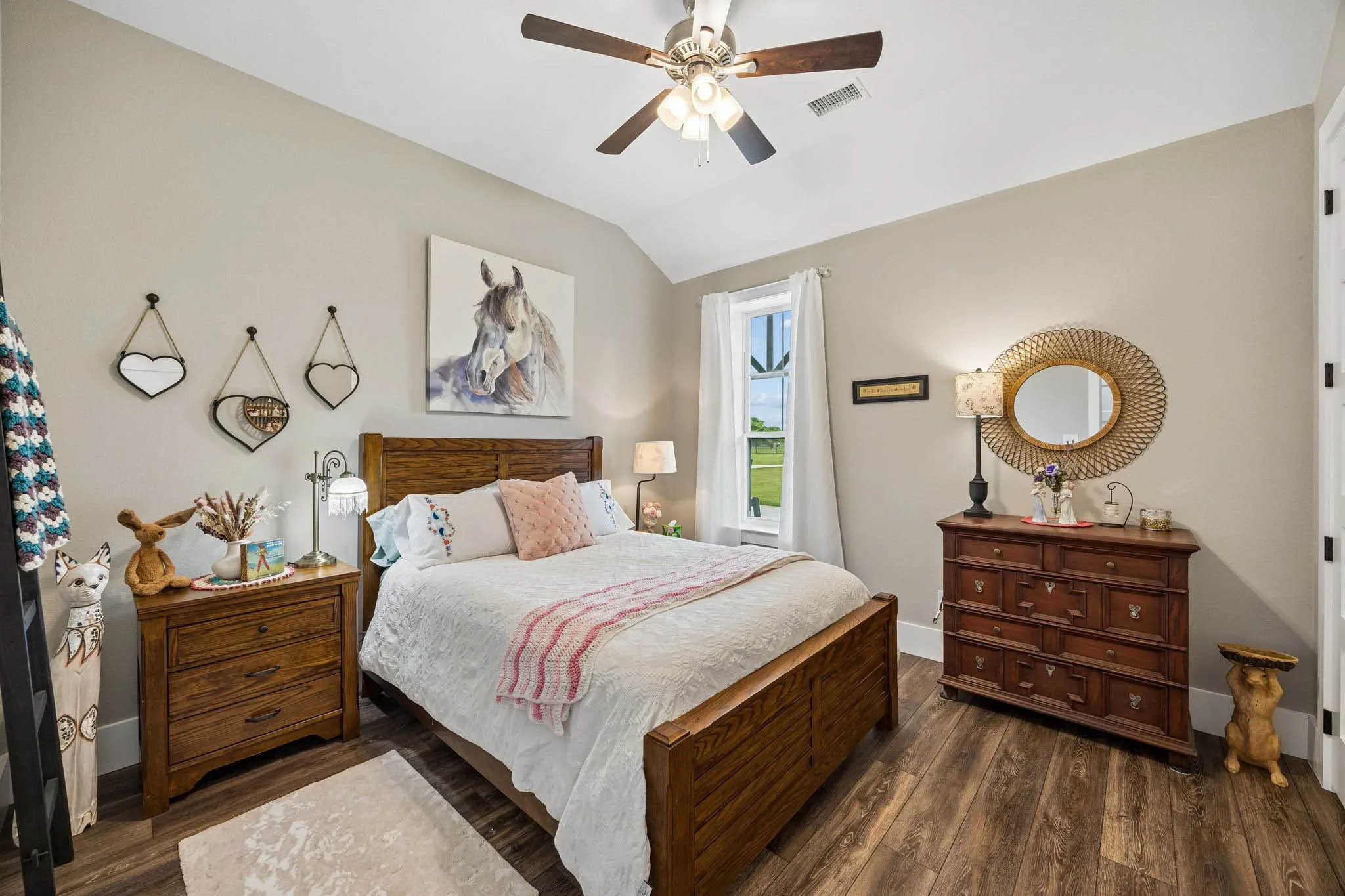 Vaulted ceiling featuring a ceiling fan, wood-finish flooring, and a window with white curtains
