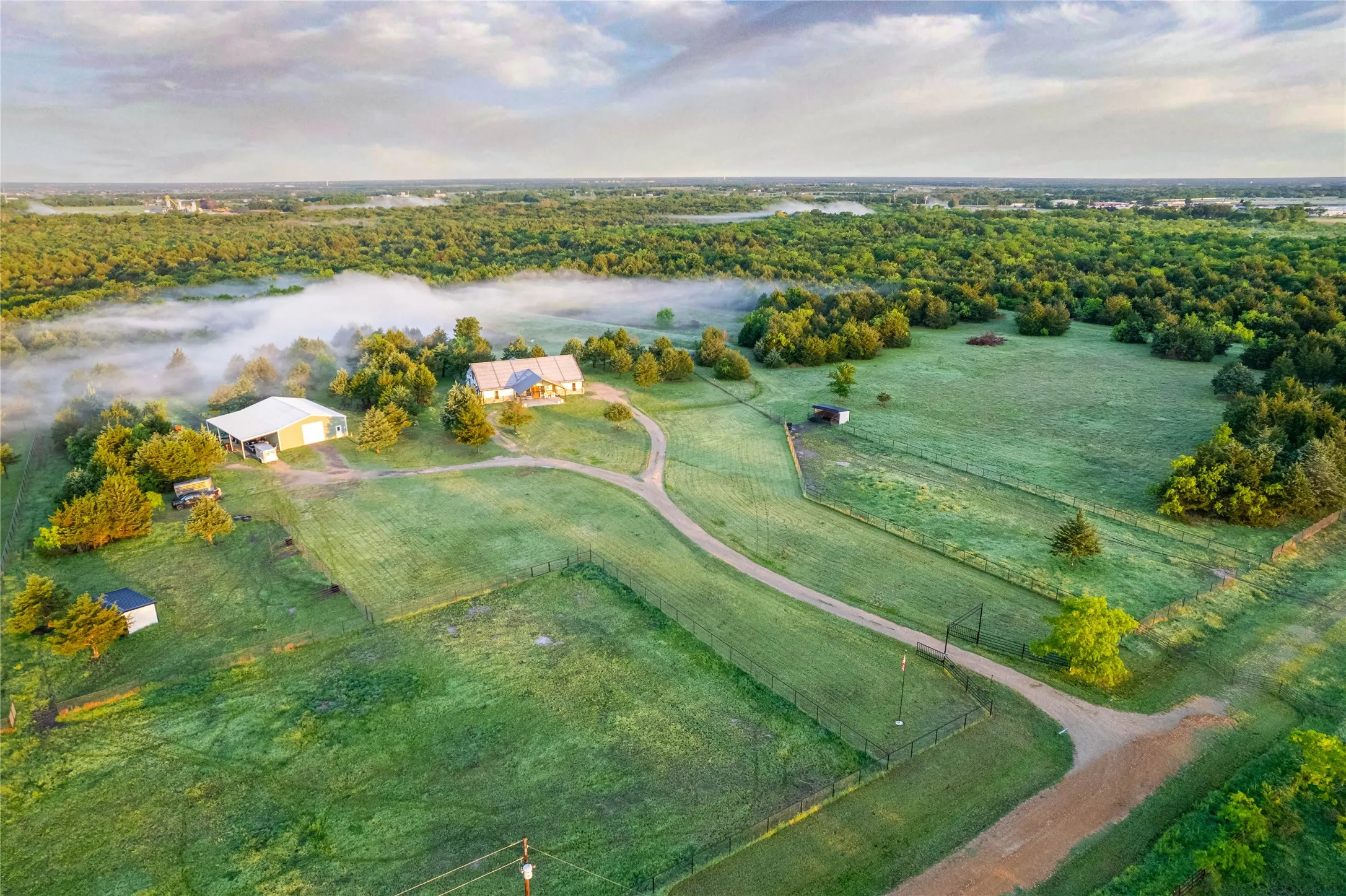 Expansive property featuring a main residence, a large outbuilding, multiple fenced areas, mature trees, and a winding driveway