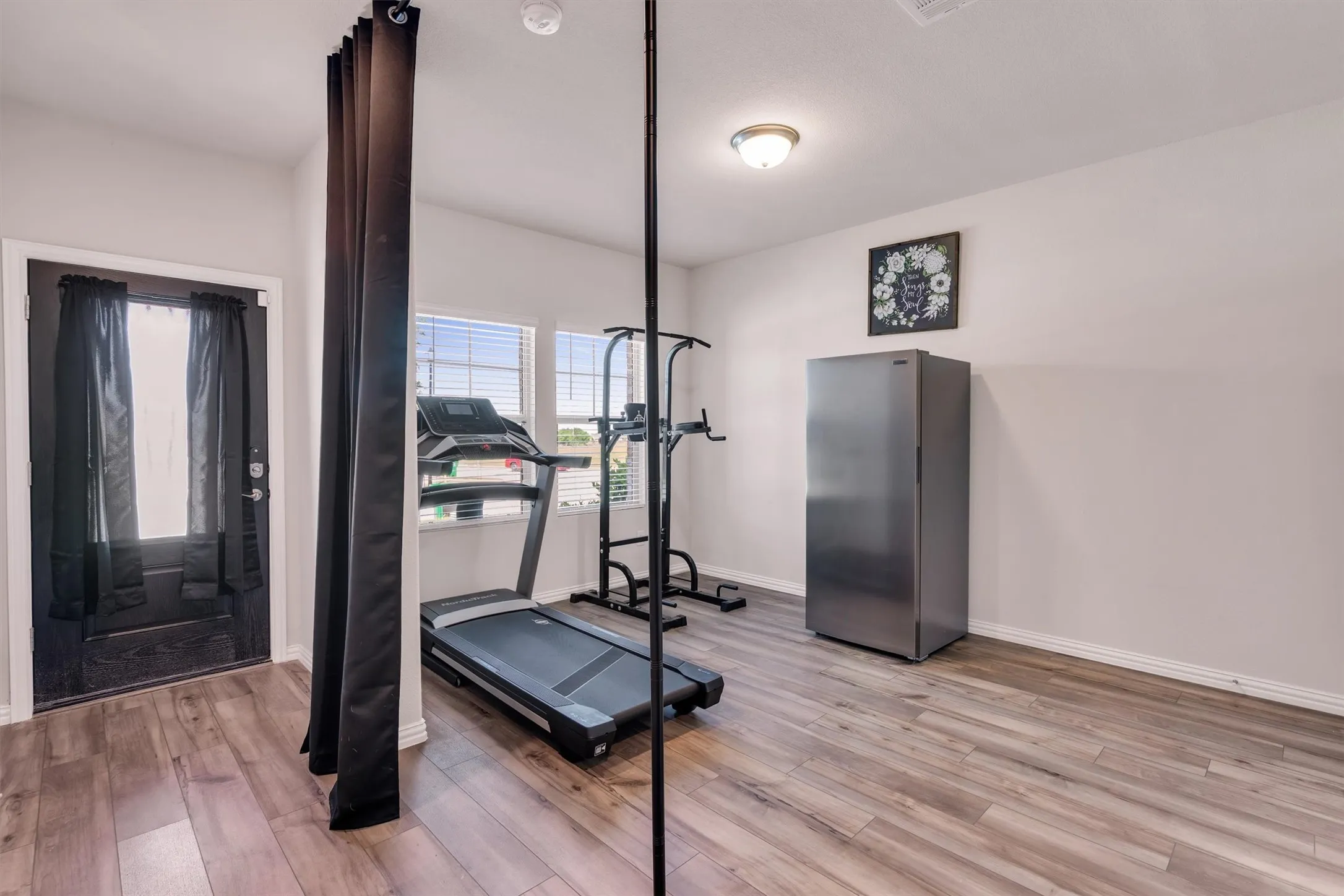 Versatile room featuring wood-finish flooring, light-toned walls, and a black exterior door with glass panels