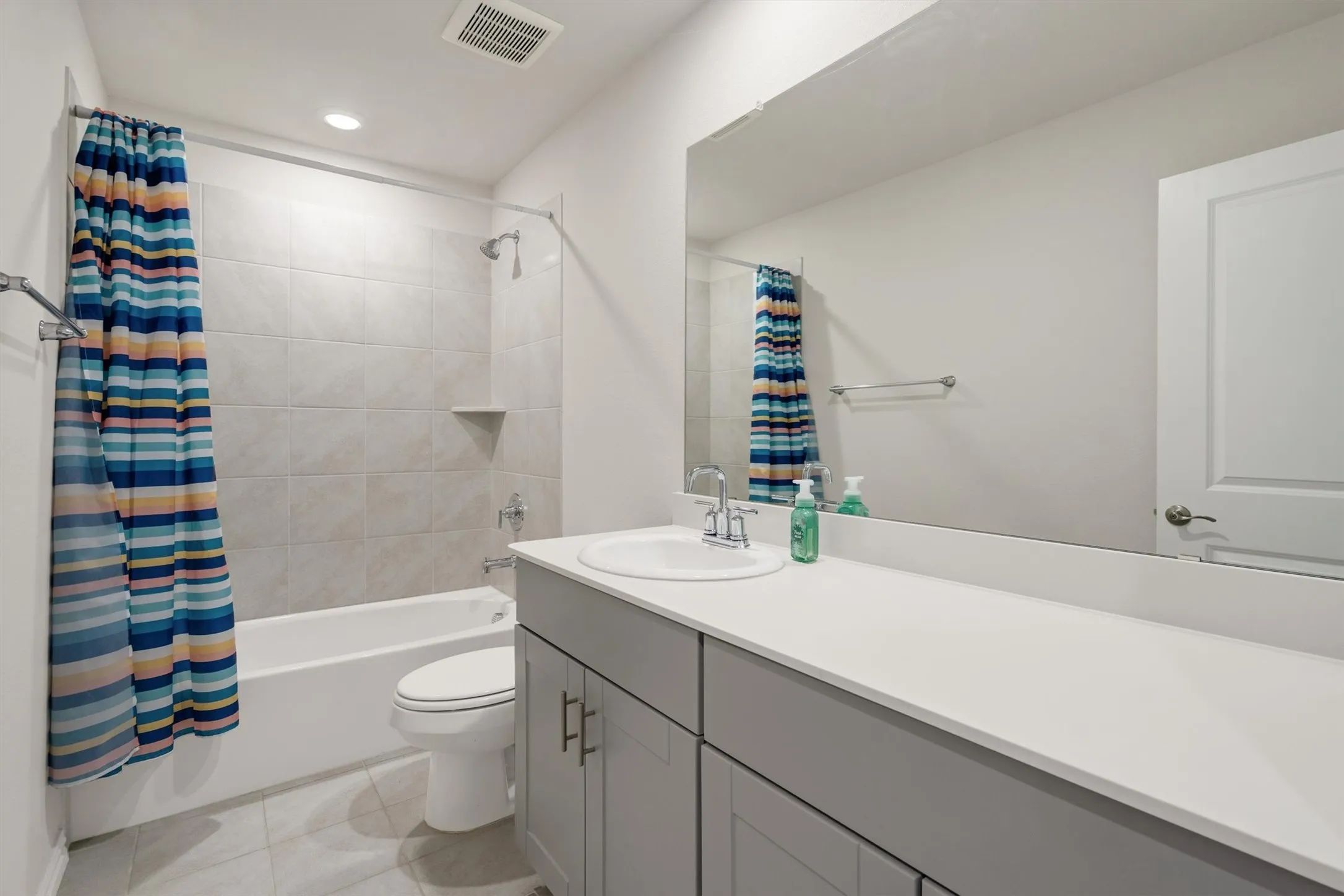 Bathroom featuring a spacious vanity with an integrated sink, a large mirror, a shower-tub combination with tile surround, and tile flooring