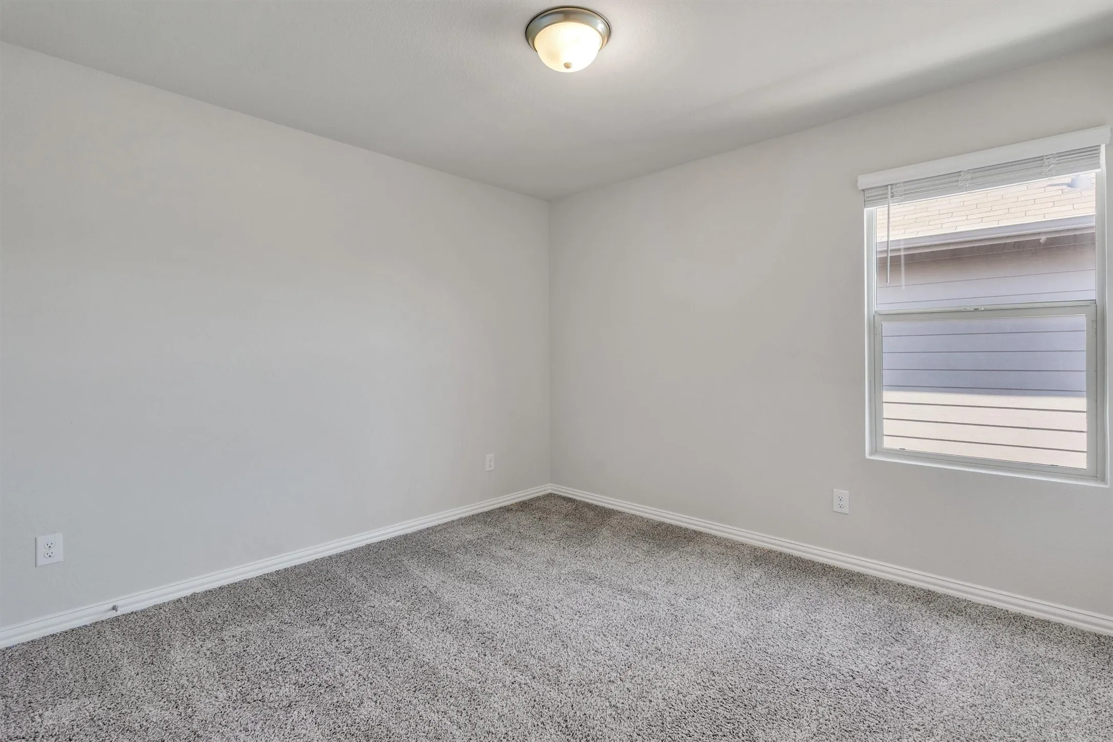 Room with neutral gray wall paint, gray carpet, white baseboards, and a single window with white blinds