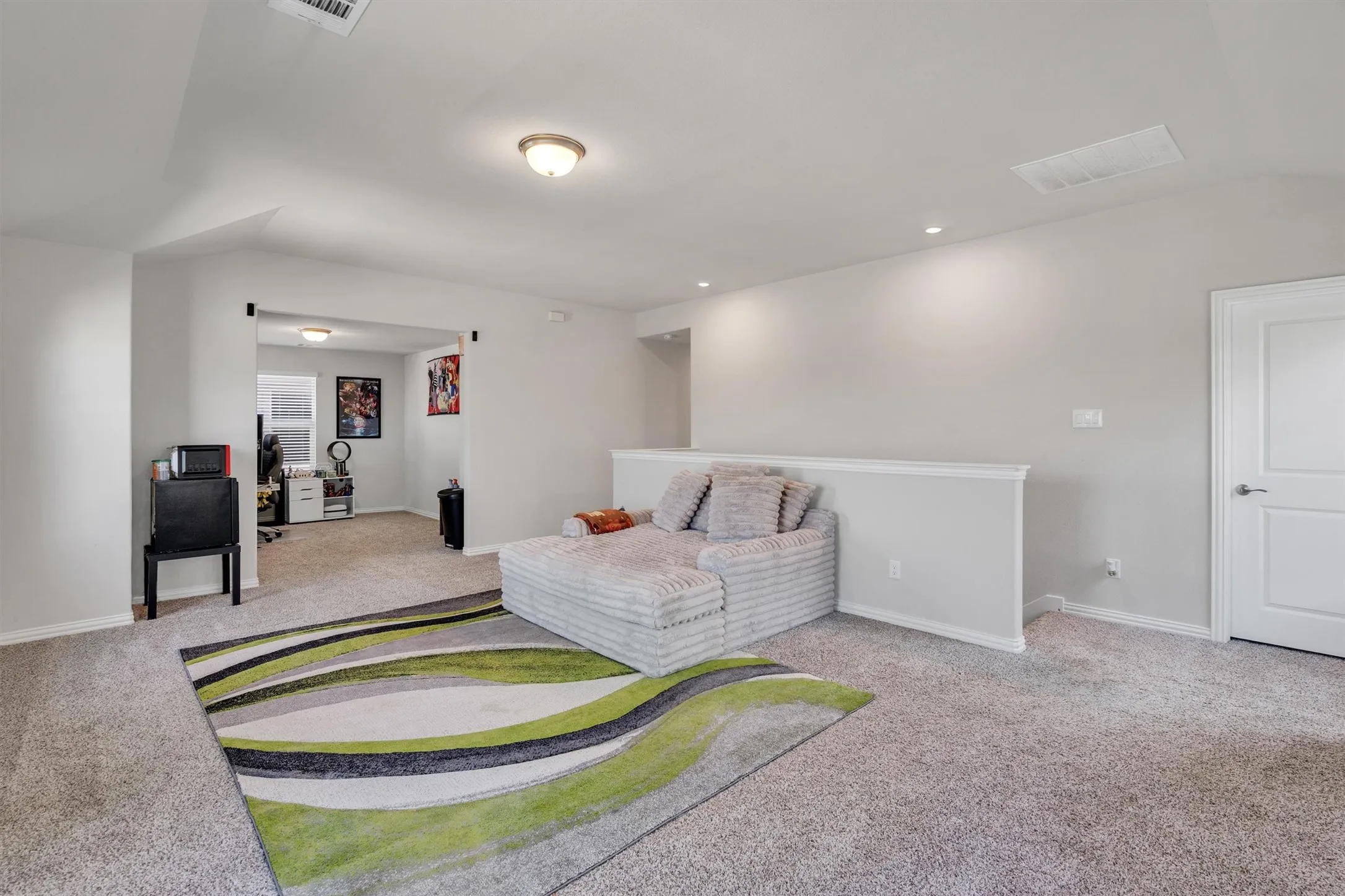 Spacious carpeted room featuring a white interior door, a half-wall partition, and an arched entryway leading to an additional space