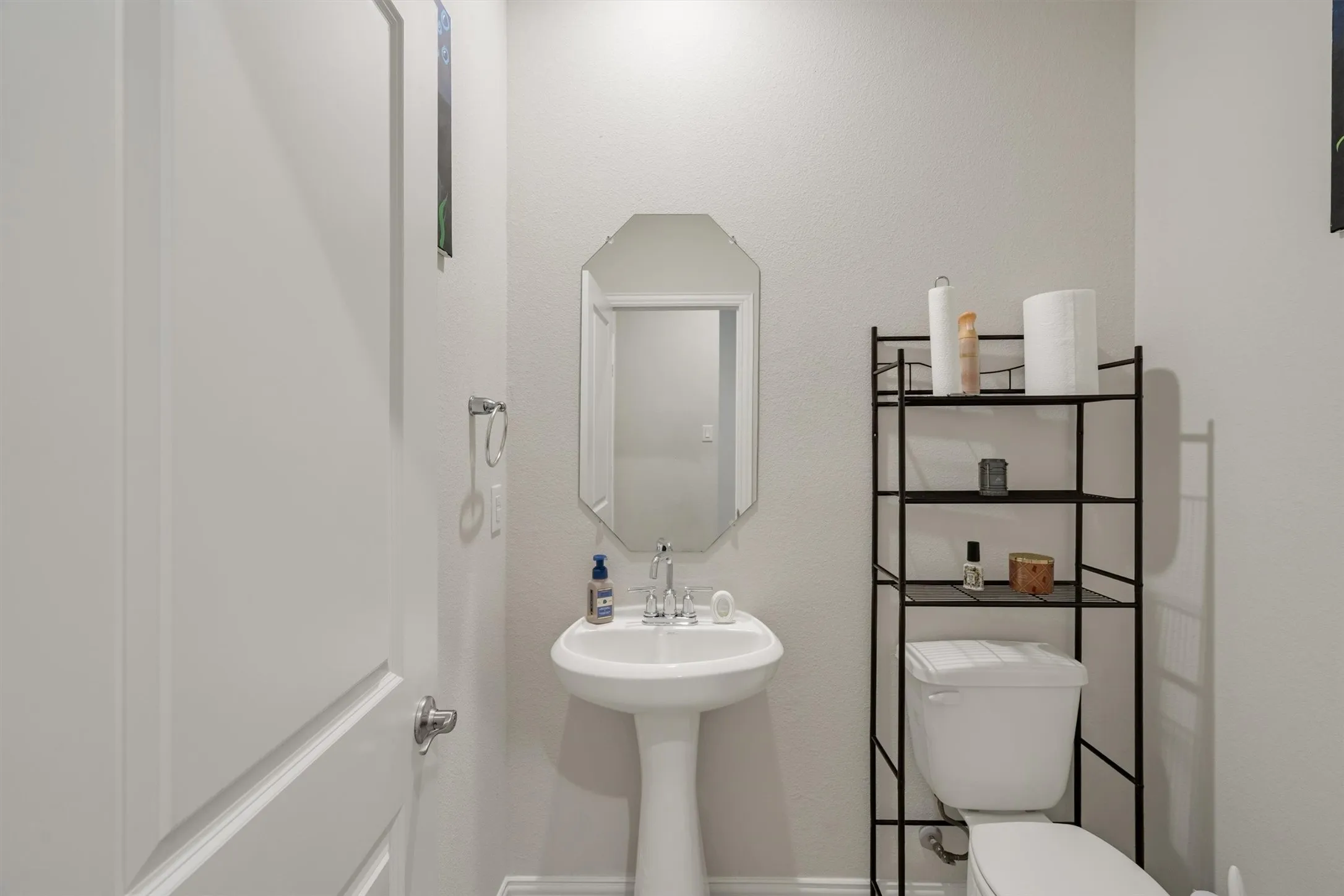 Pedestal sink with chrome faucet, octagonal mirror, and light gray wall paint