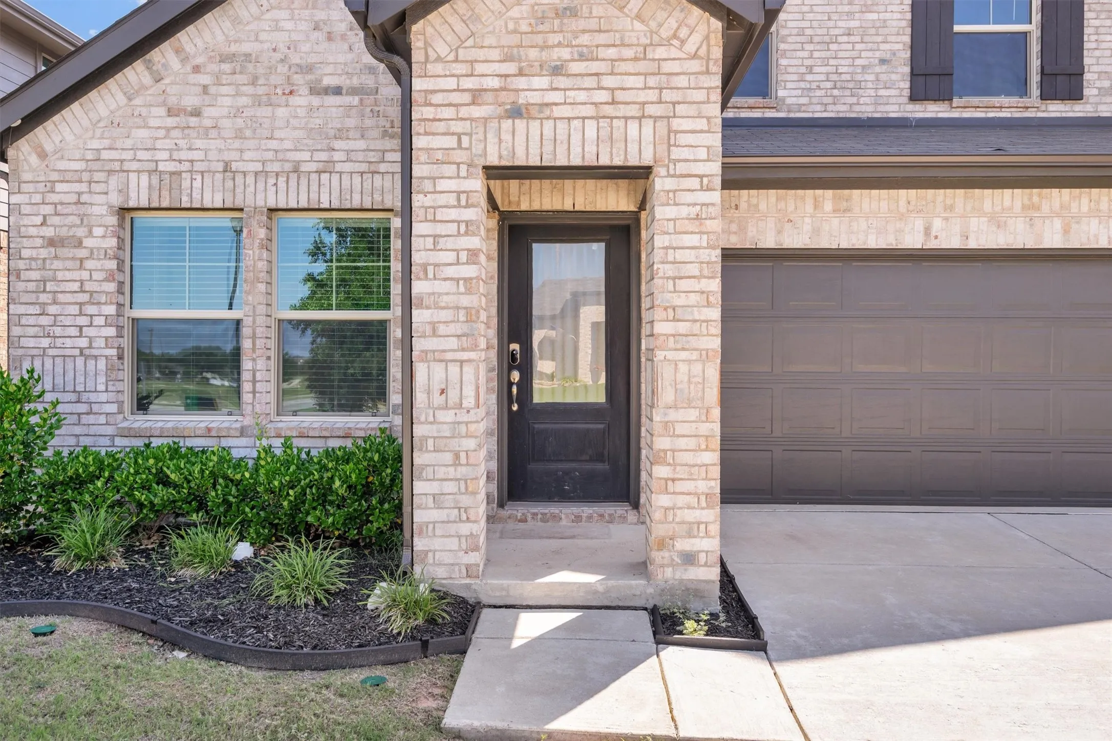 Light brick exterior with dark trim and a prominent two-car garage