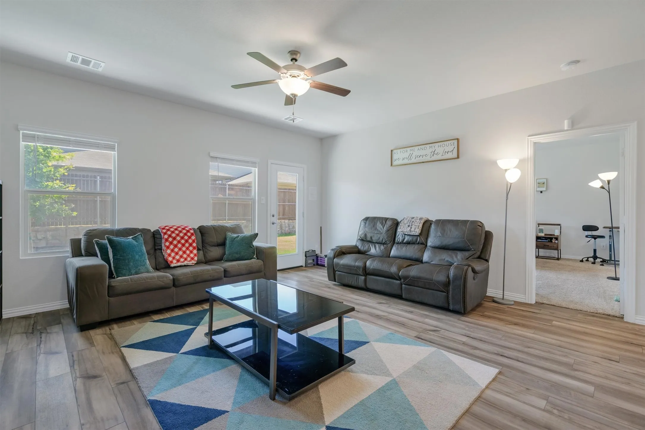 Spacious living area featuring wood-finish flooring, light grey wall paint, and a ceiling fan with integrated lighting