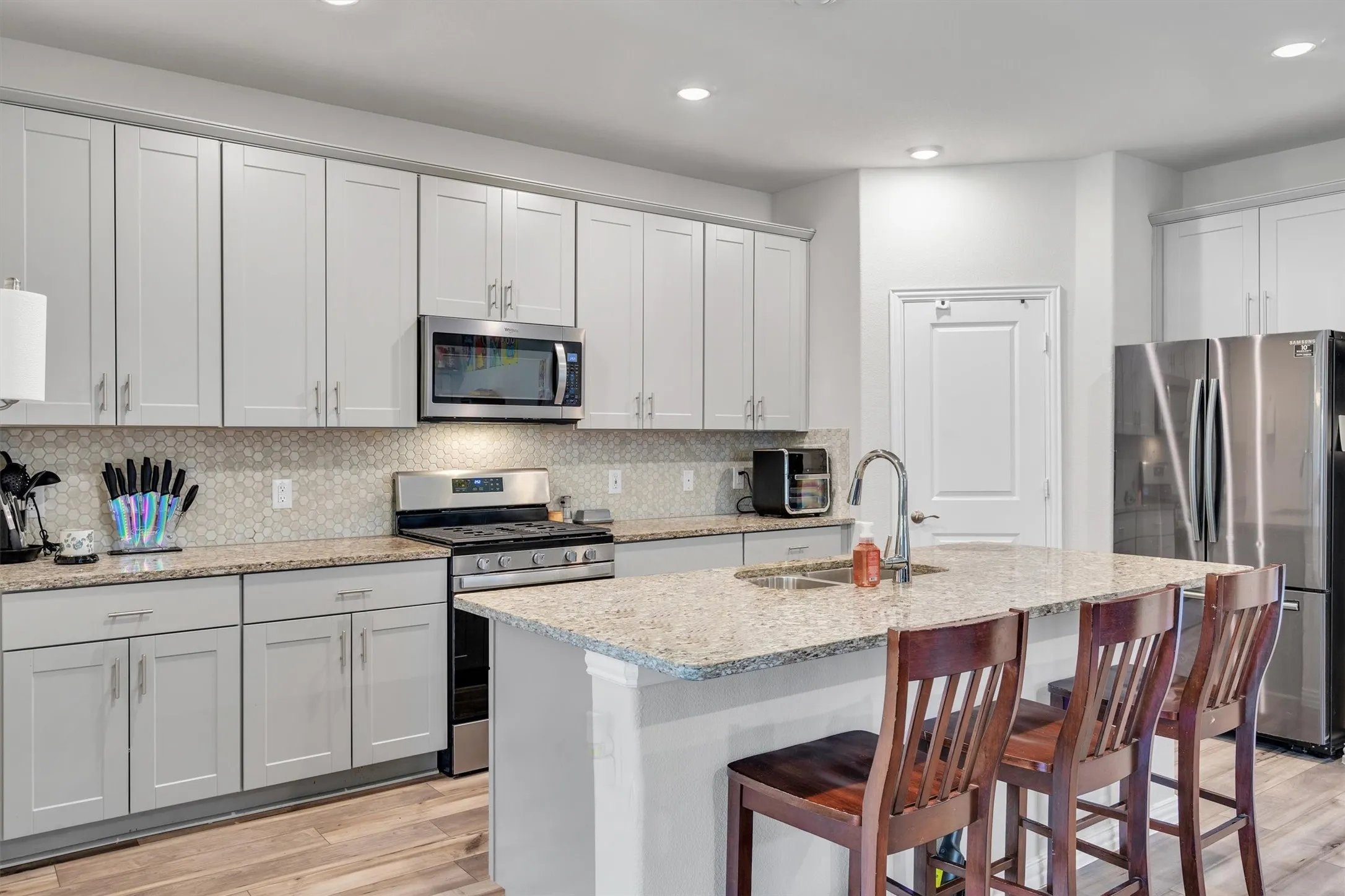 Contemporary kitchen featuring light gray shaker cabinetry, stainless steel appliances, a tiled backsplash, and granite countertops