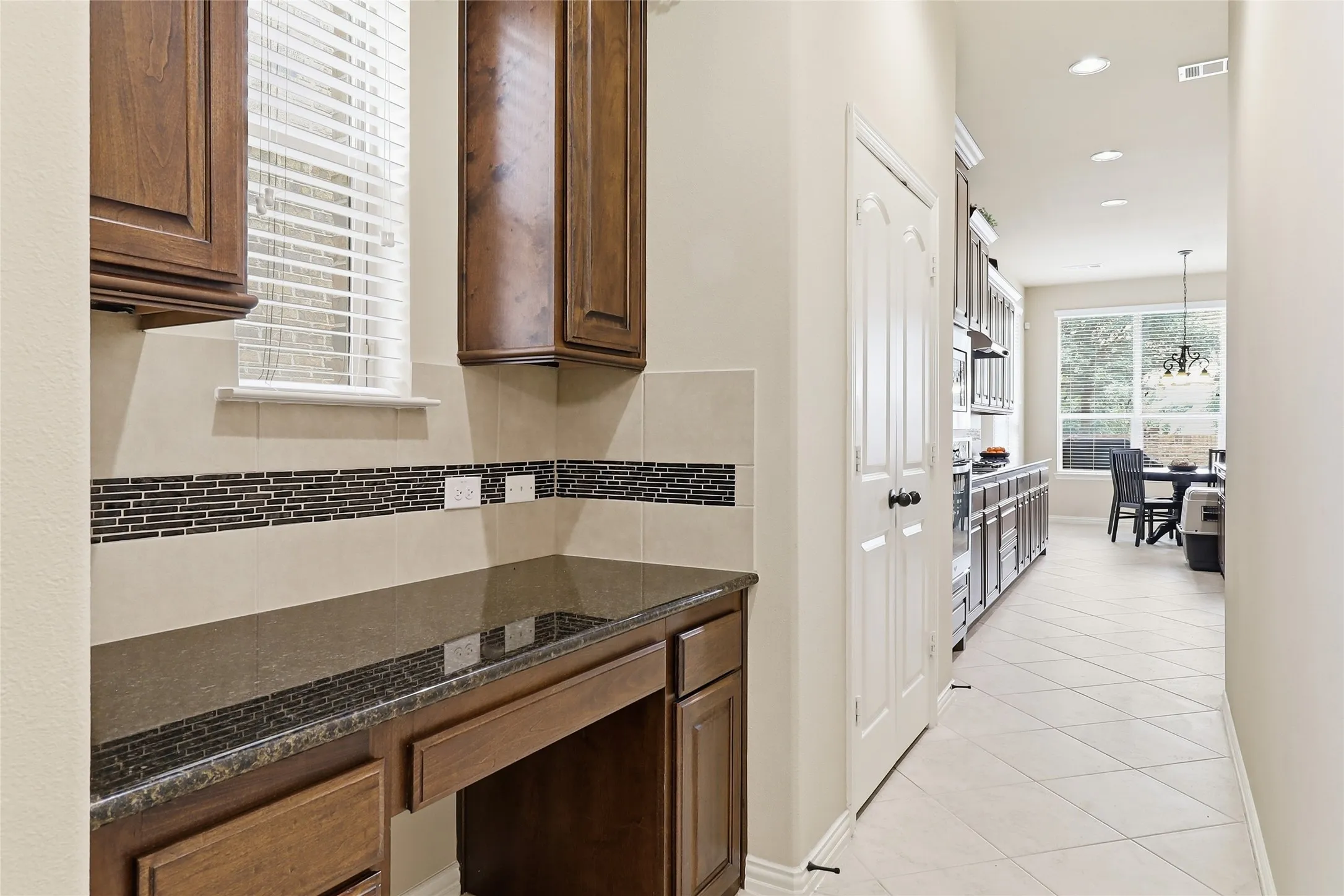 Built-in desk area featuring wood cabinetry, a dark countertop, and a tiled backsplash with a decorative mosaic accent