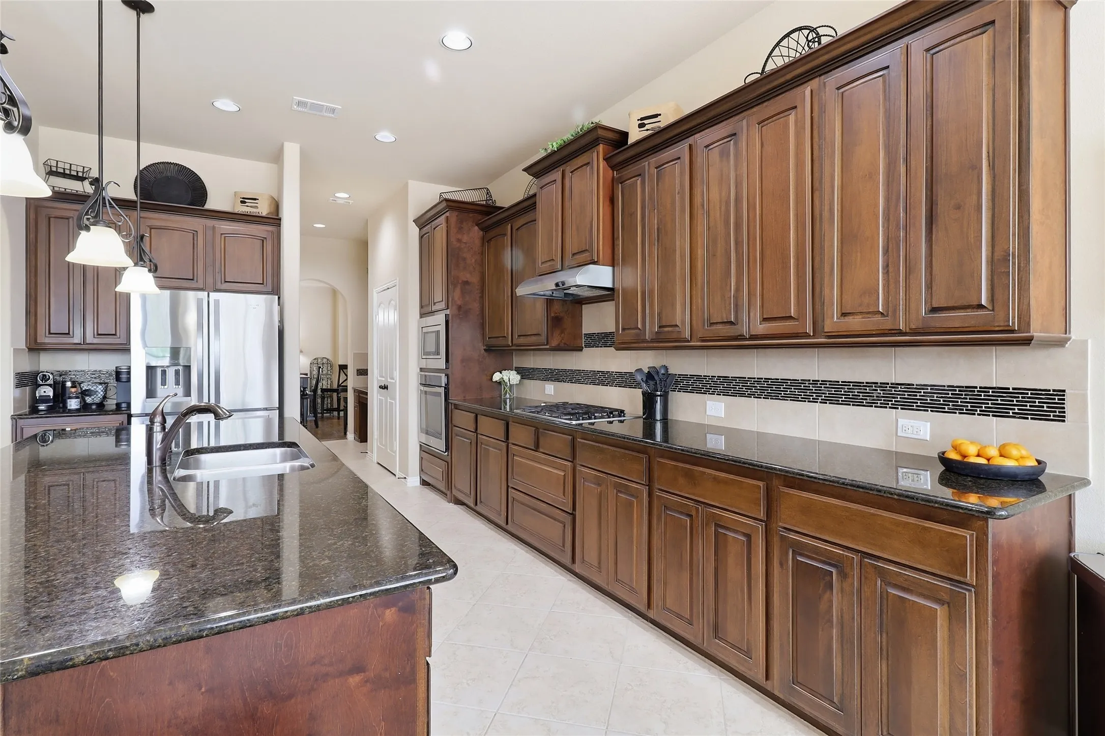 Spacious kitchen featuring extensive dark wood cabinetry, granite countertops, stainless steel appliances, a tile backsplash with decorative accent, and recessed lighting