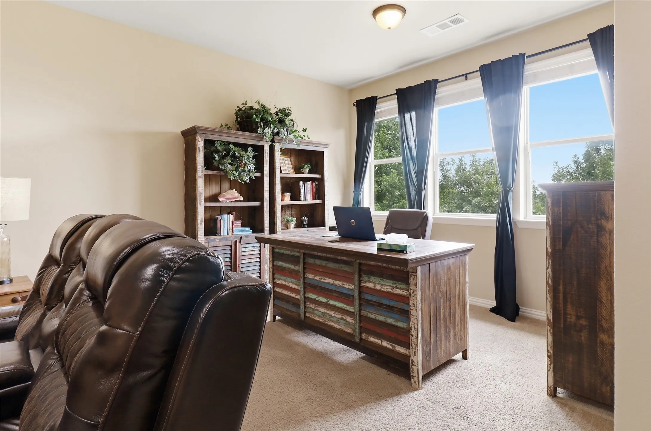 Bright room featuring multiple windows with tree-lined scenery, beige wall tones, and carpet flooring