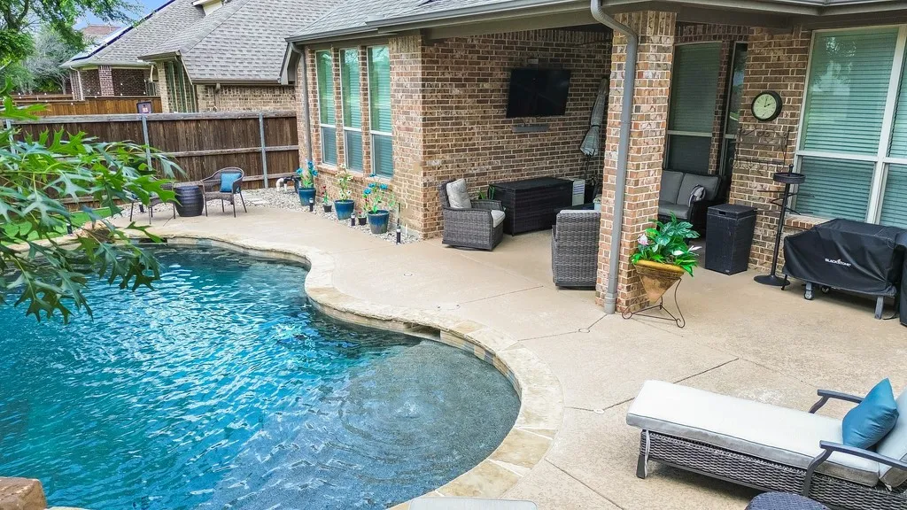 Curved in-ground pool with stone coping and an expansive concrete patio