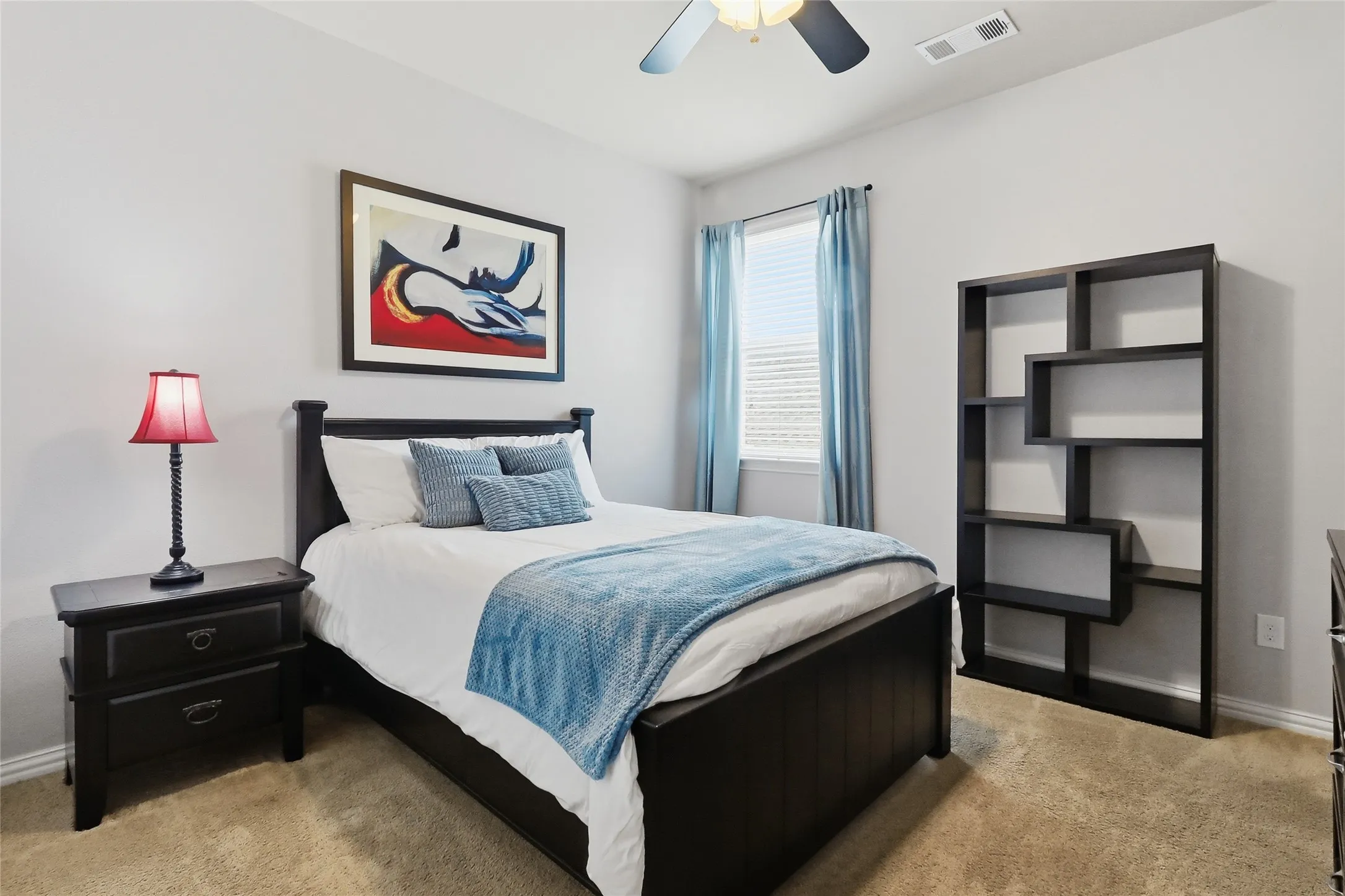 Carpeted room with a ceiling fan, featuring light gray walls and a single window with blinds and blue drapes