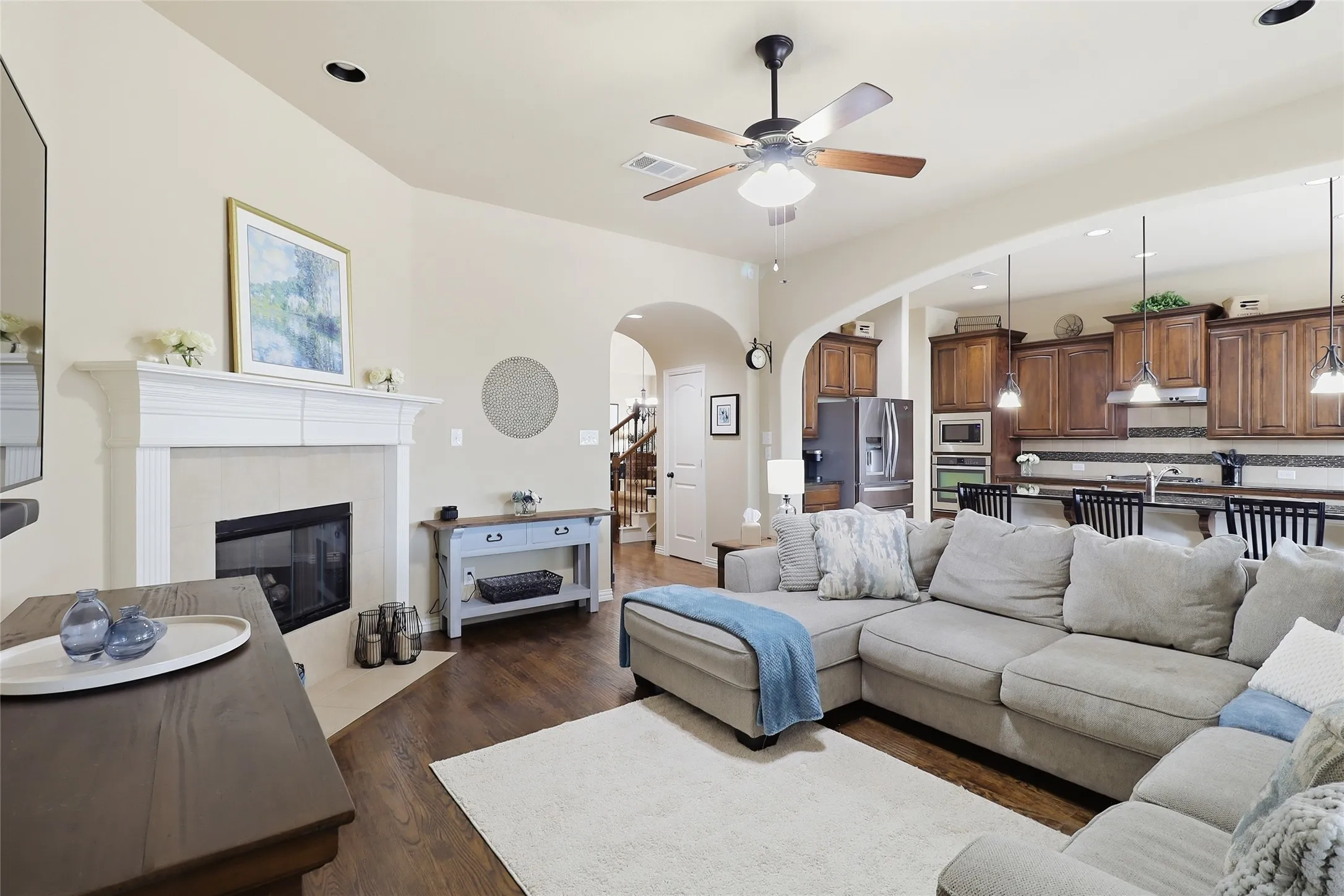 Open-concept living area featuring a fireplace with a white mantel, wood-finish flooring, and recessed lighting