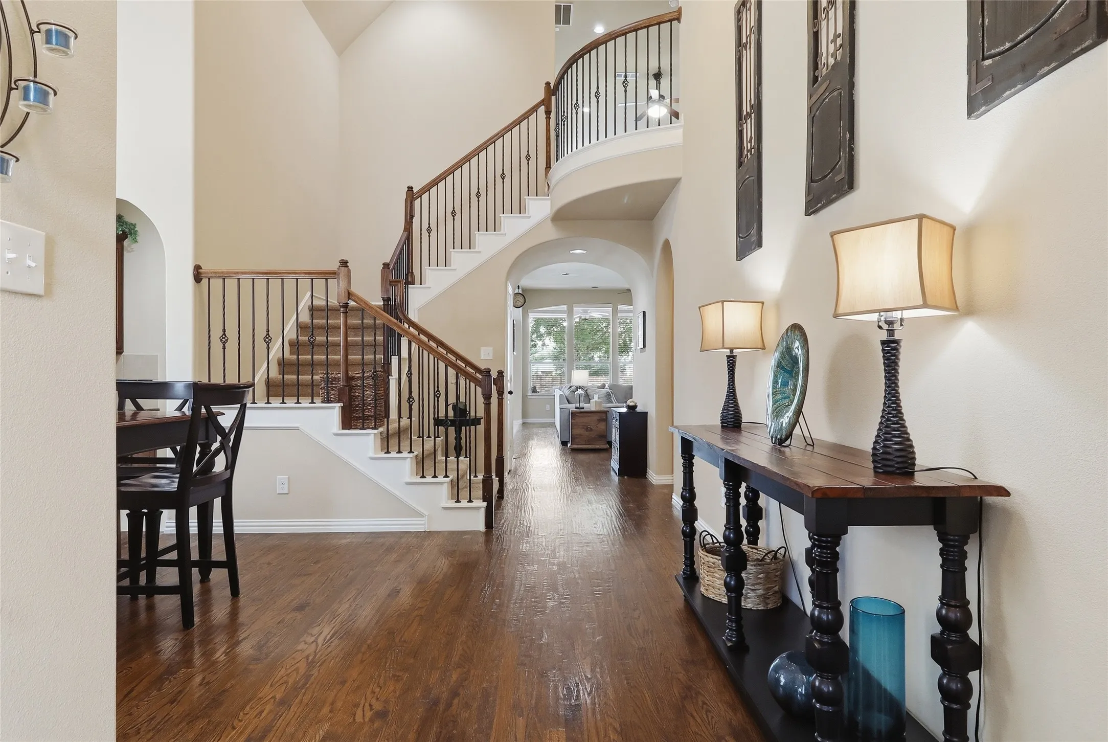 Two-story foyer featuring wood-finish flooring, a grand staircase with wrought iron balusters and wood handrails, and arched doorways