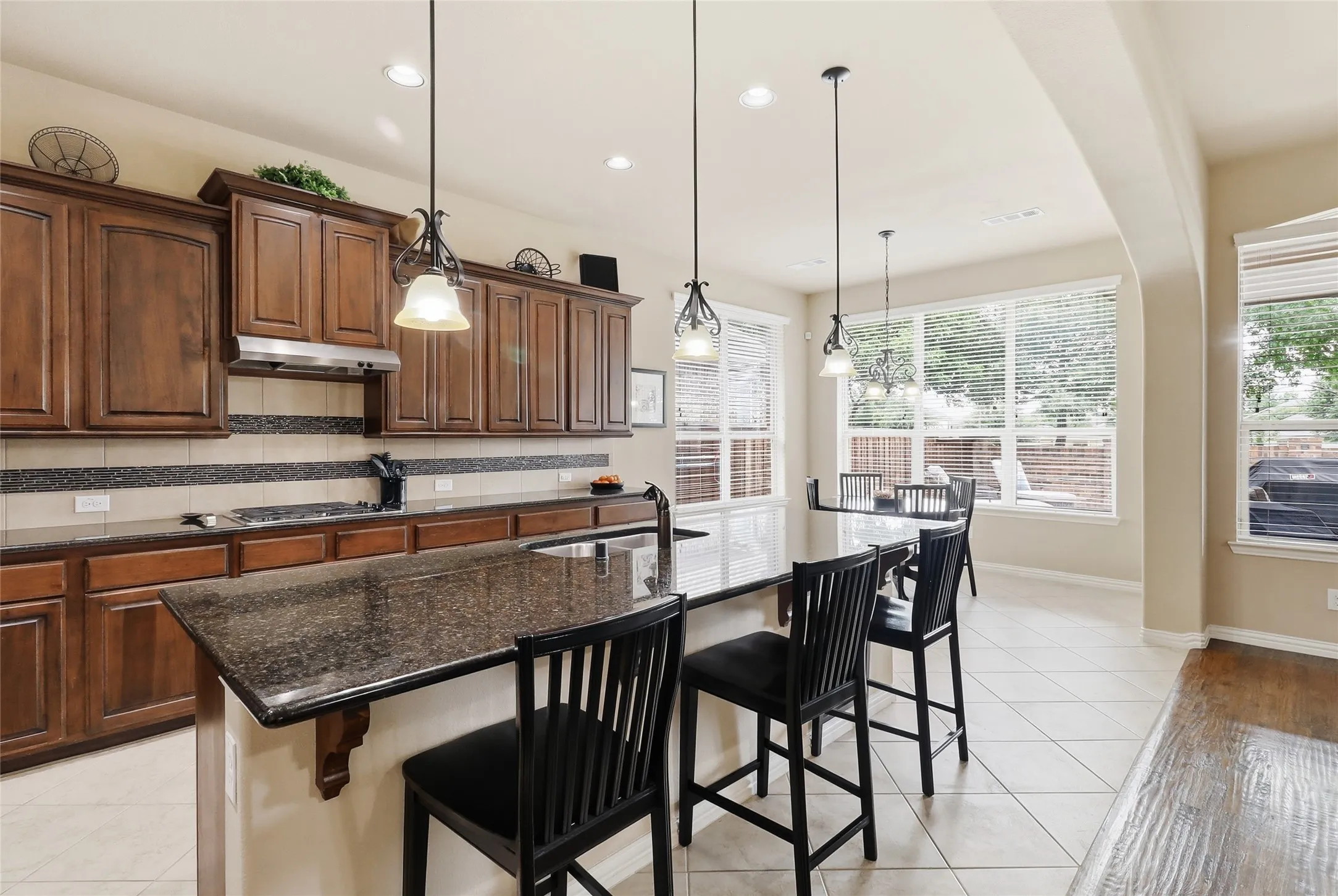 Kitchen featuring wood cabinetry, dark countertops, tile flooring, pendant lighting, and multiple windows