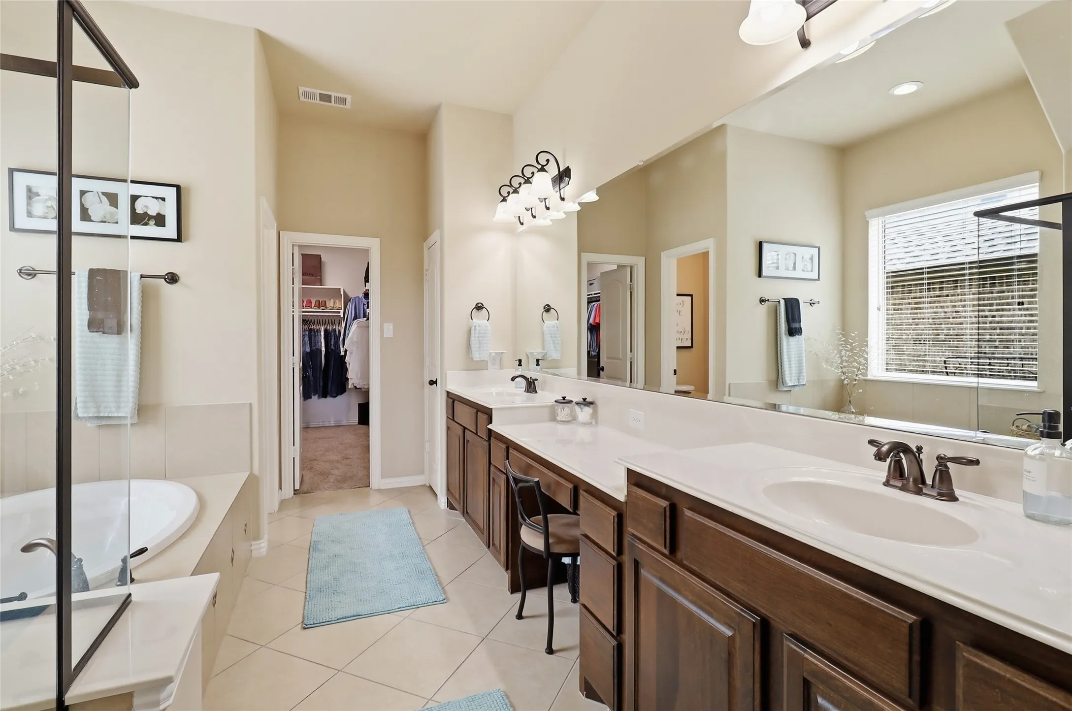 Bathroom featuring a dual vanity with white countertops and dark wood cabinetry, a built-in soaking tub, a separate glass-enclosed shower, and tile flooring