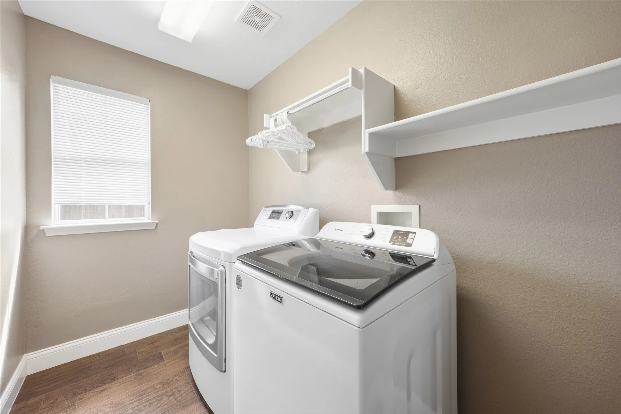 Laundry room featuring wood-finish flooring, a window with blinds, and built-in shelving with a hanging rod