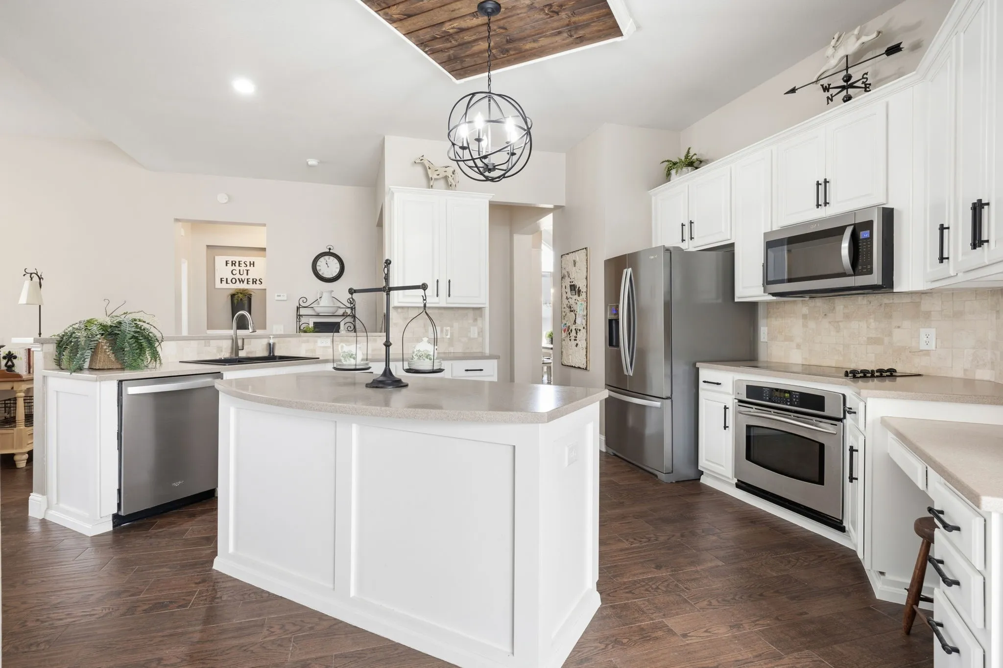 Kitchen featuring a central island with a light-toned countertop, white cabinetry with dark hardware, stainless steel appliances, wood-finish flooring, and a decorative wood-paneled ceiling accent