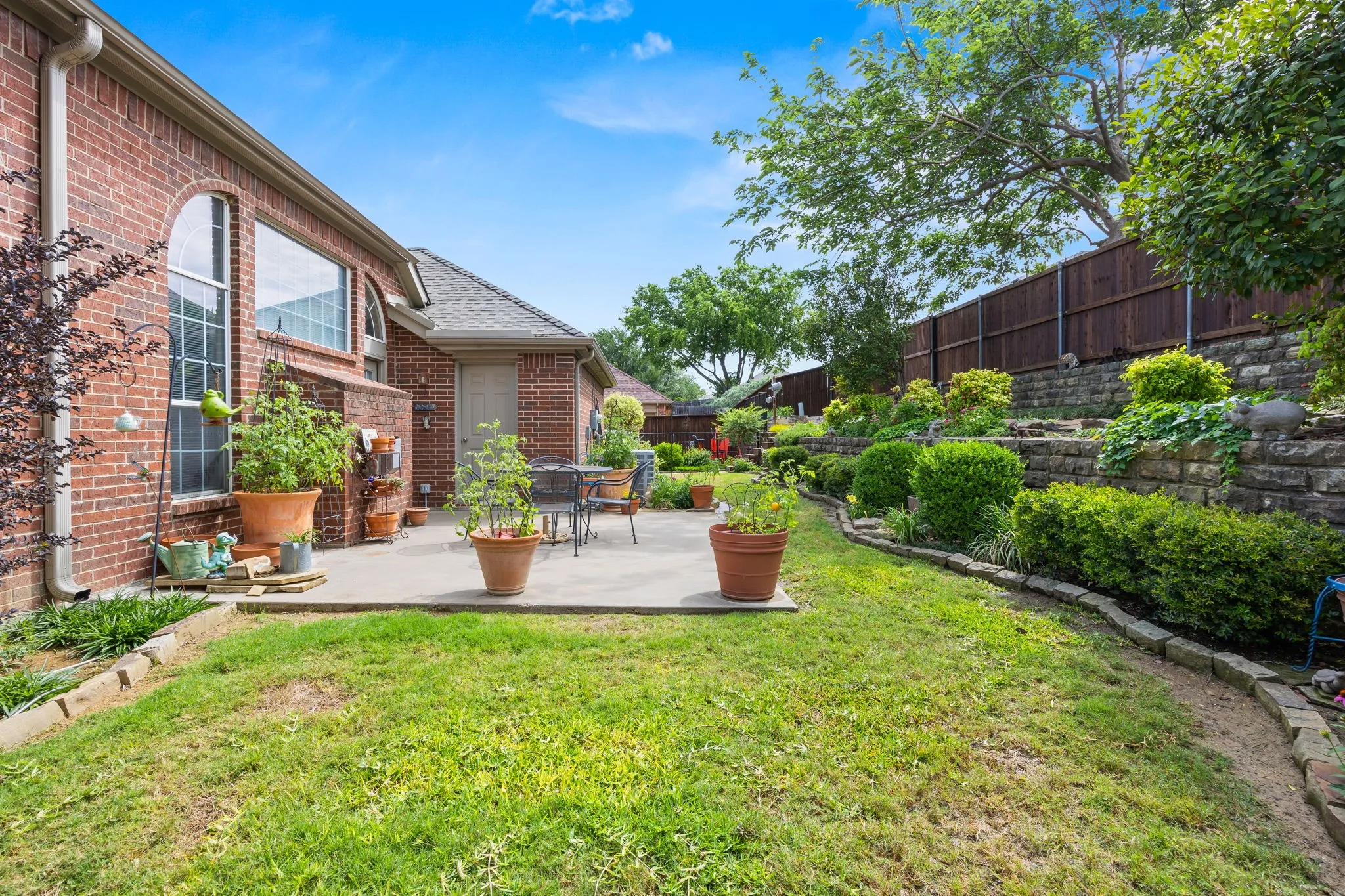 Expansive backyard featuring a concrete patio, a red brick exterior, and tiered landscaping with stone retaining walls