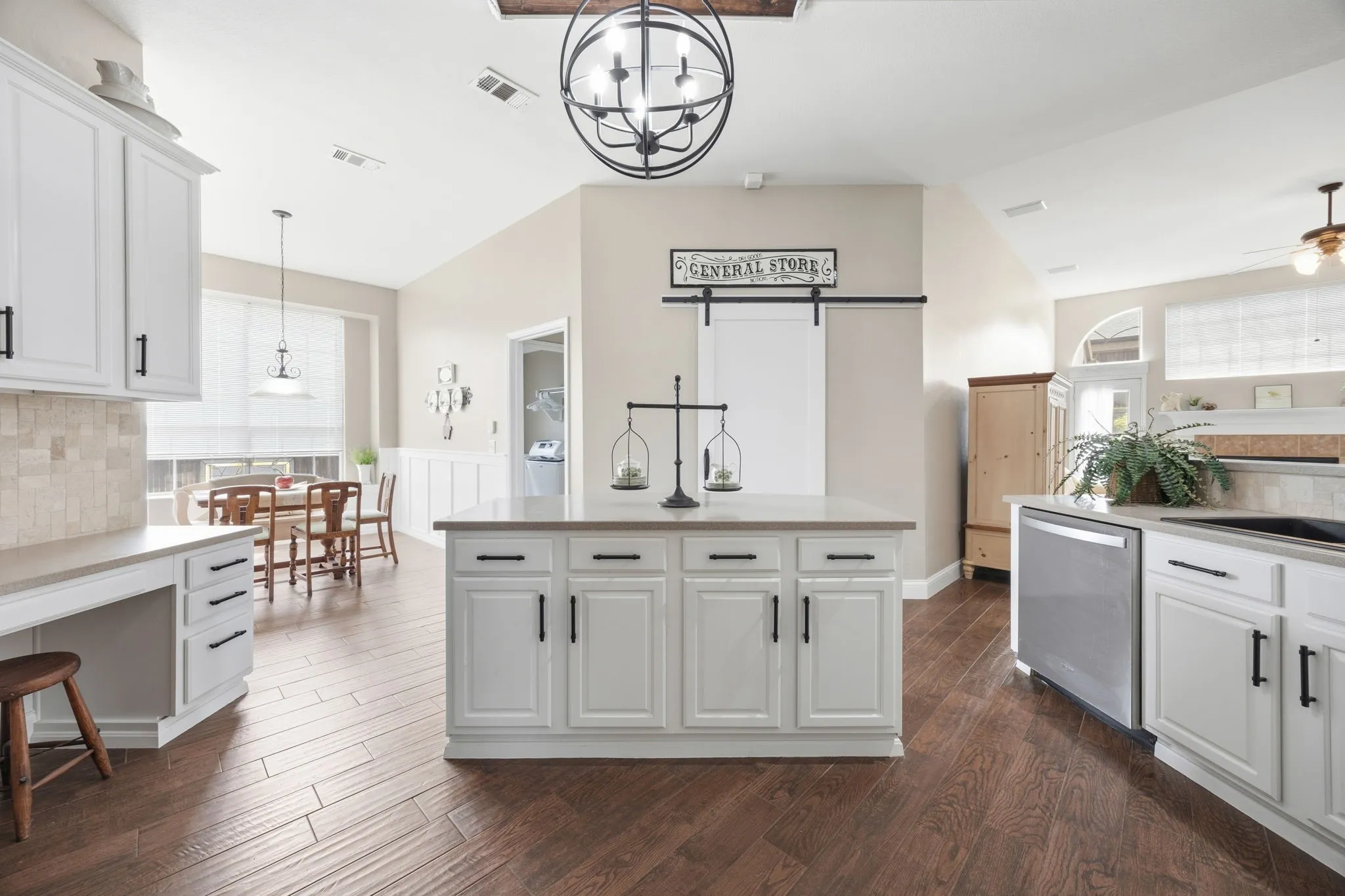 Spacious kitchen featuring white cabinetry, a central island with a light-colored countertop, dark wood-finish flooring, and stainless steel appliances