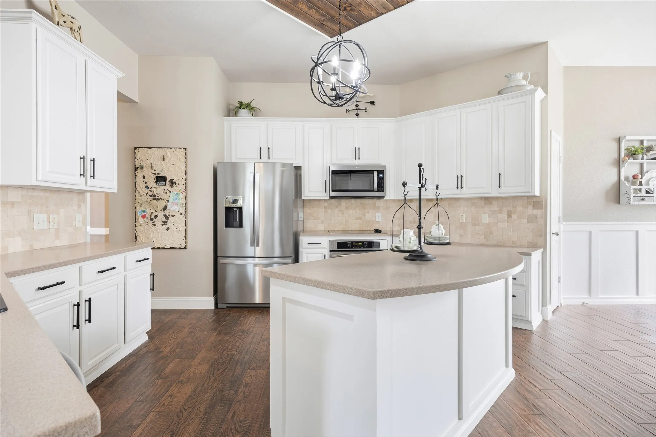 Contemporary kitchen featuring white cabinetry, a neutral-toned backsplash, stainless steel appliances, a center island with countertop seating, and wood-finish flooring
