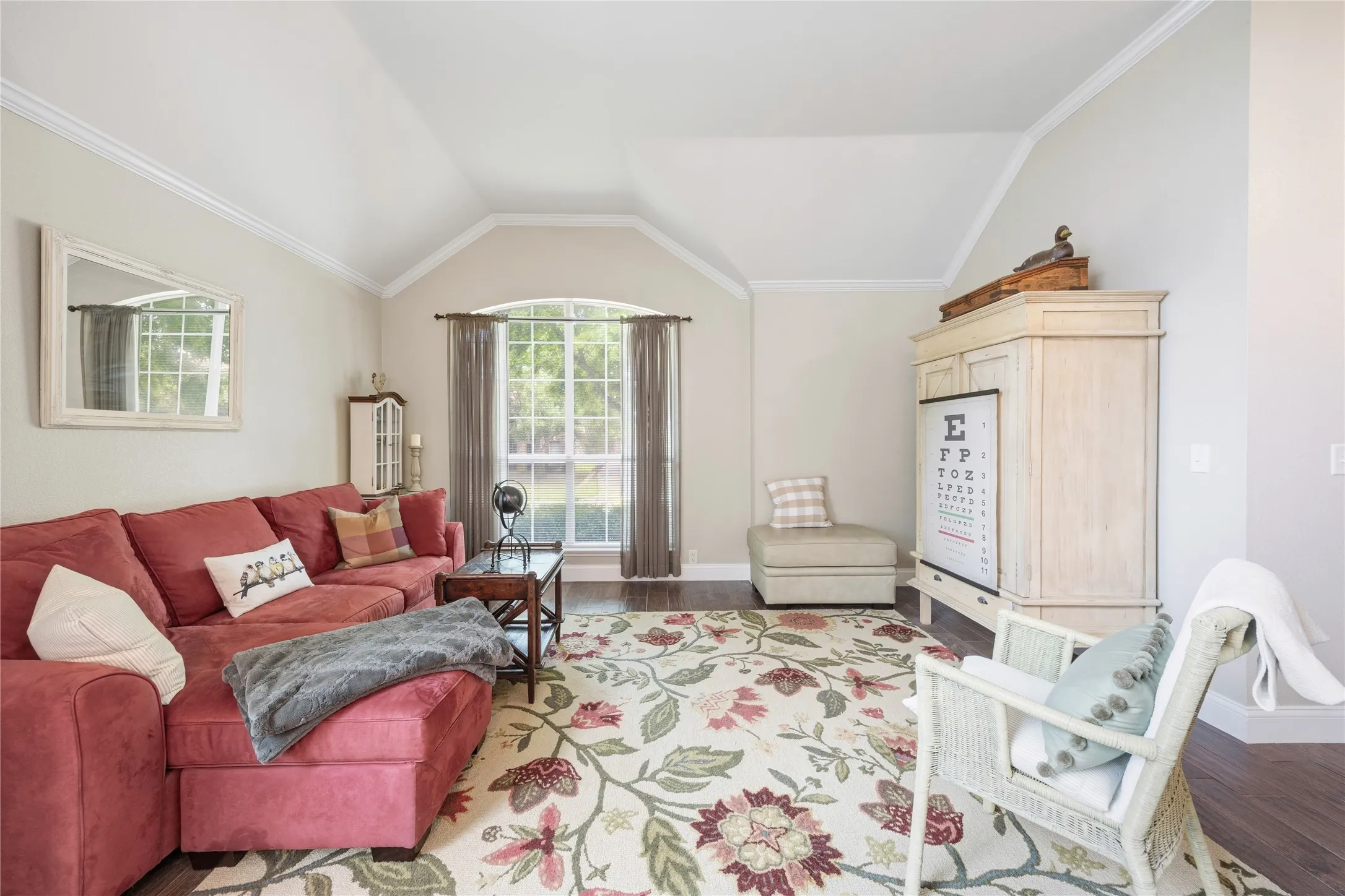 Vaulted ceilings with crown molding, arched window with grid pattern, wood-finish flooring, and neutral wall tones