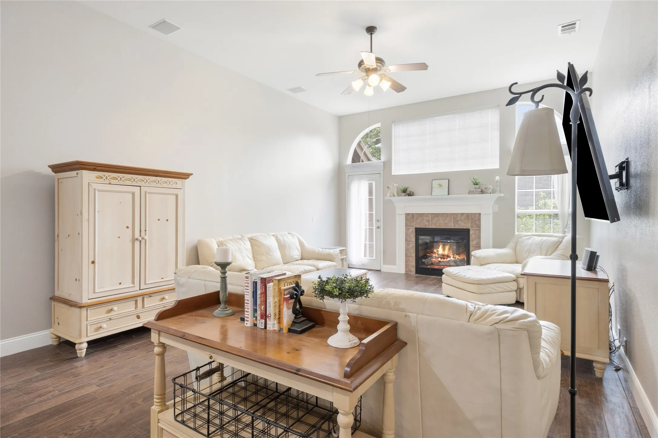Spacious living area featuring wood-finish flooring, a fireplace with a light-colored mantel, a ceiling fan, vaulted ceilings, and recessed lighting
