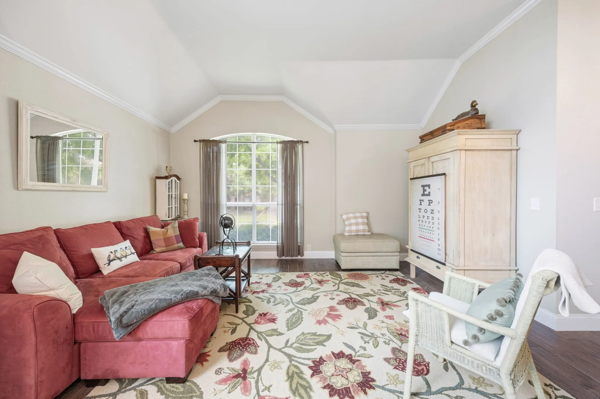 Vaulted ceiling great room featuring crown molding, a large arched window with grid details, and rich wood-finish flooring