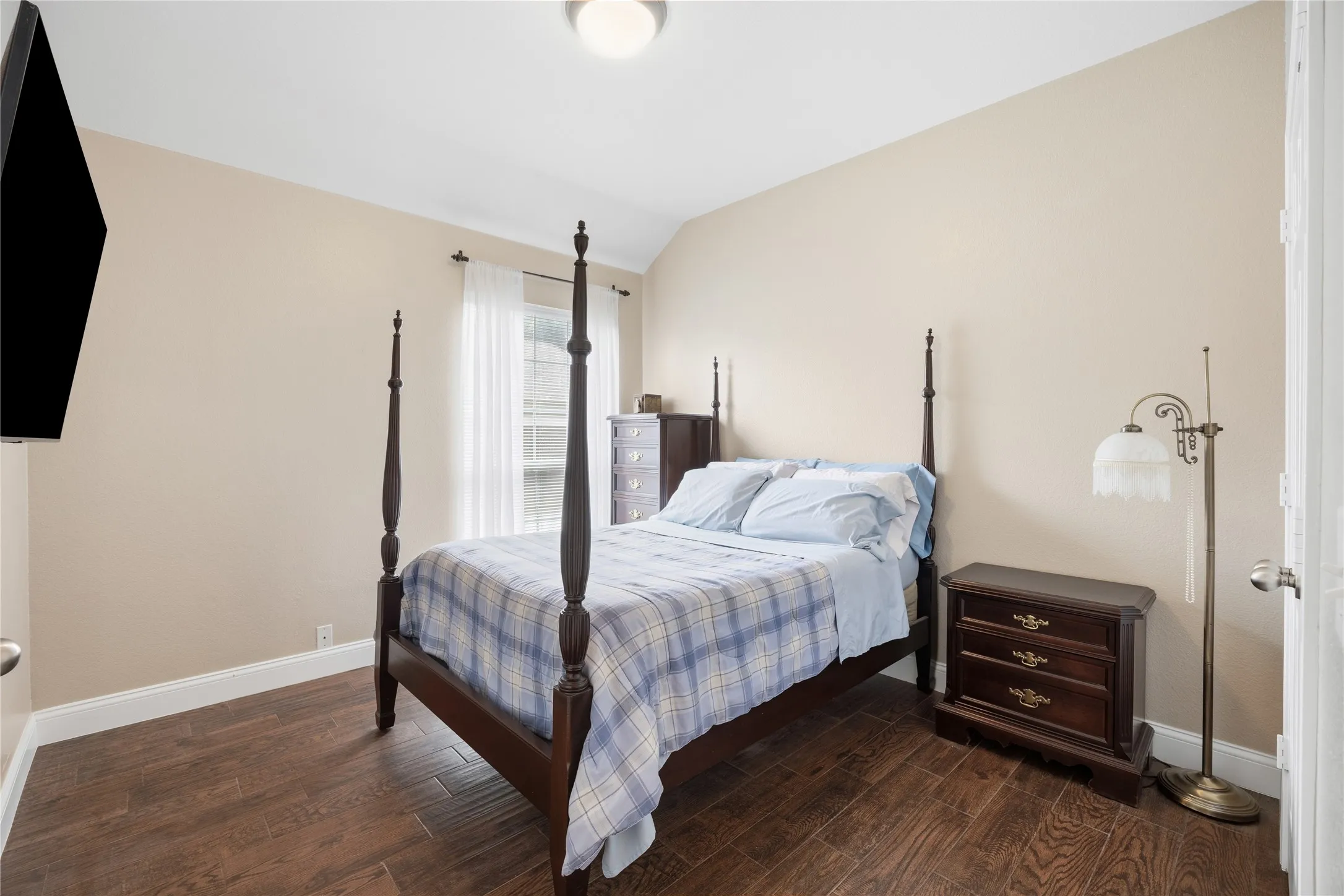 Spacious room featuring wood-finish flooring, neutral wall tones, a ceiling light fixture, and a window with white sheer curtains