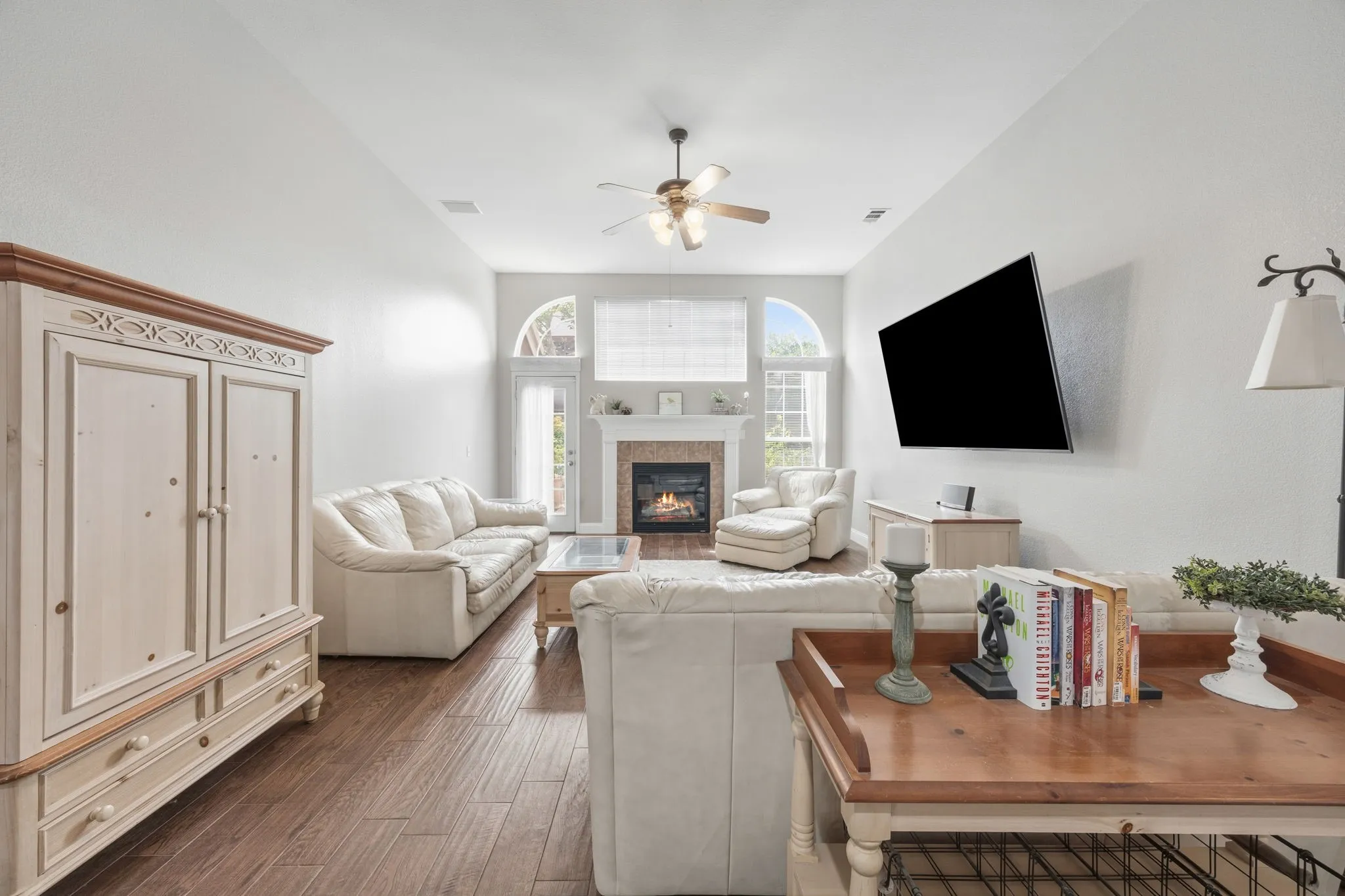 Spacious living area featuring wood-finish flooring, a fireplace with a stone surround and mantel, arched windows, and vaulted ceilings