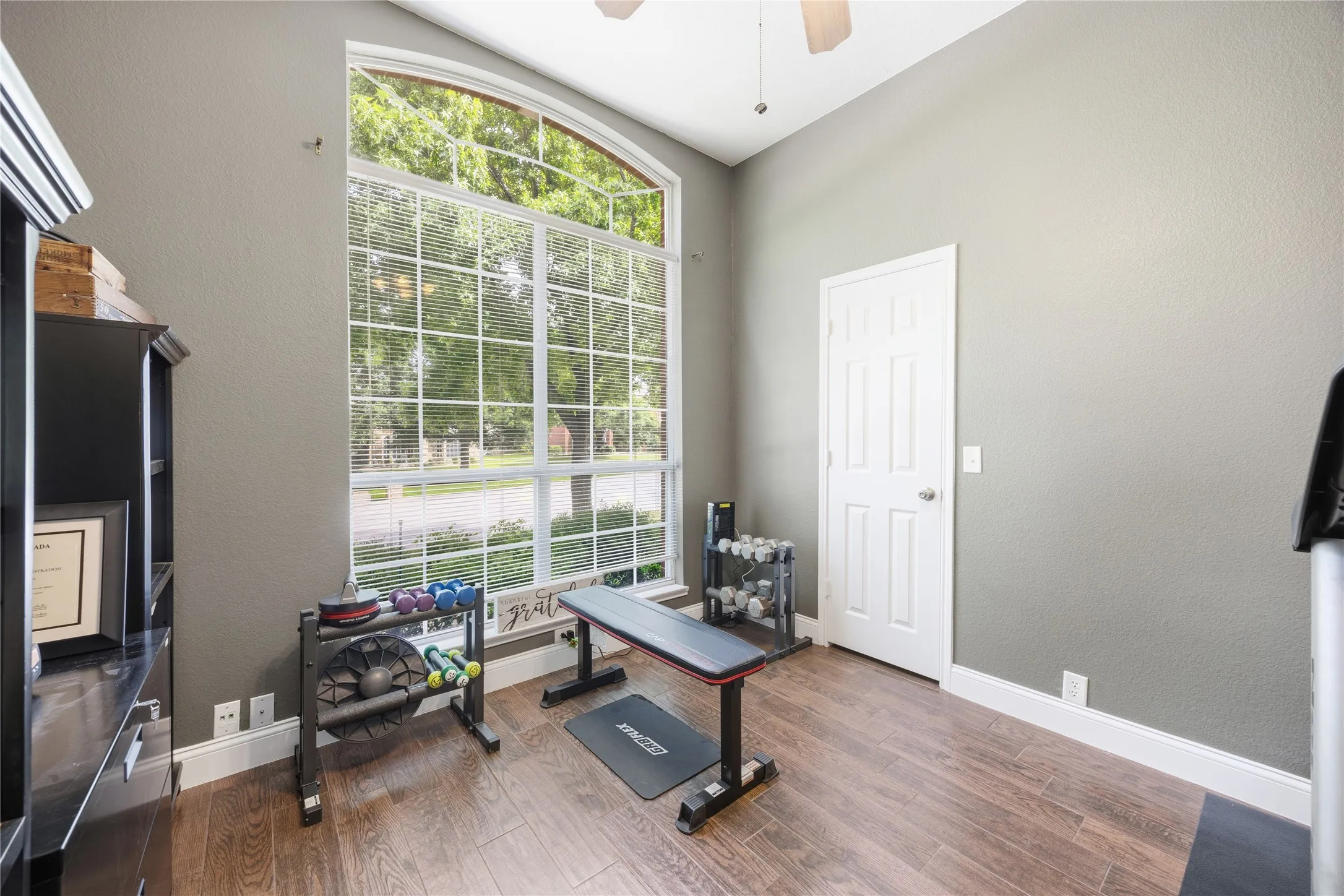 Room featuring a large arched window with grid patterns, wood-finish flooring, a paneled door, and a ceiling fan