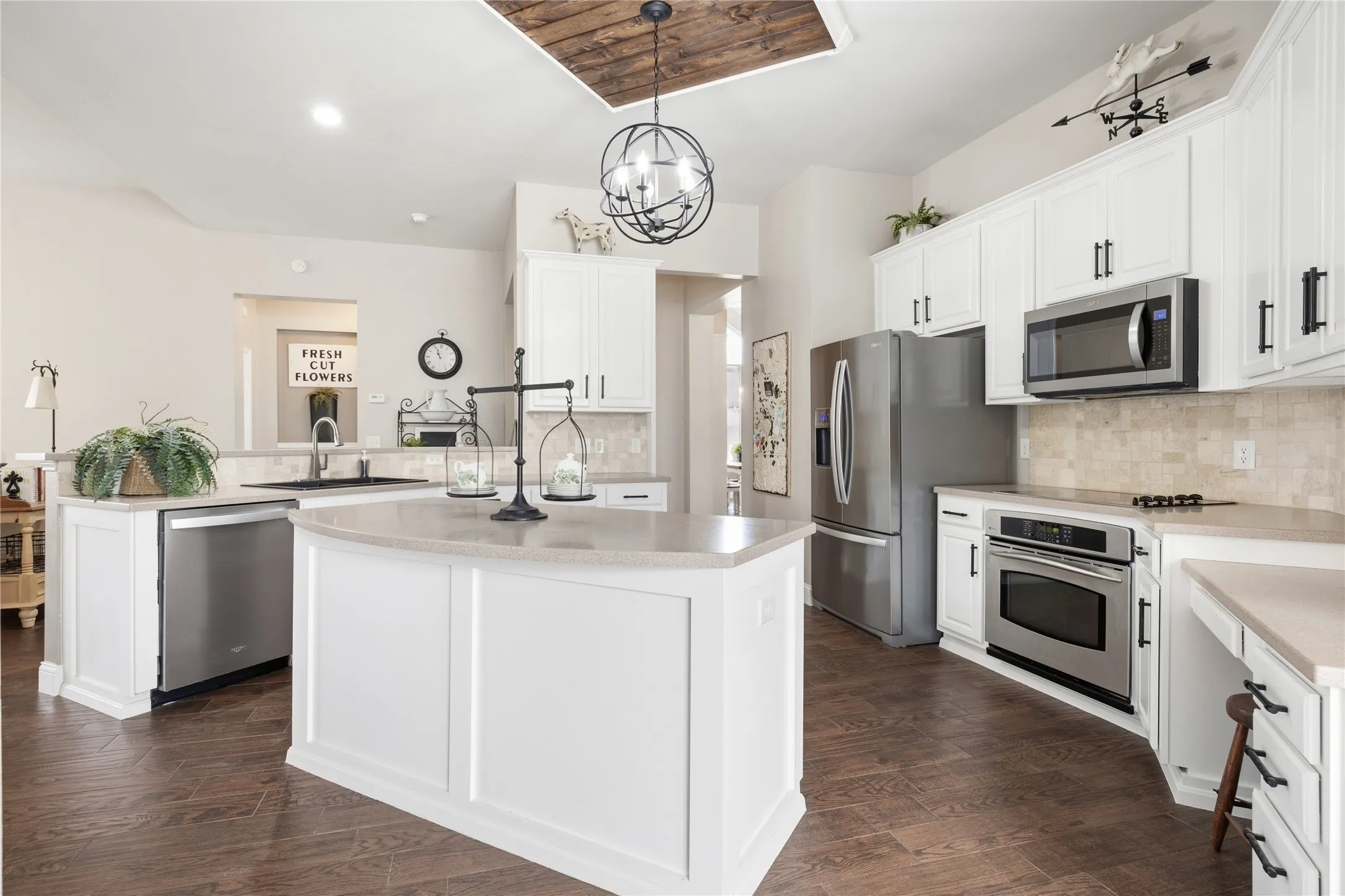 Kitchen featuring a central island, white cabinetry, integrated stainless steel appliances, wood-finish flooring, and a unique wood-paneled ceiling accent