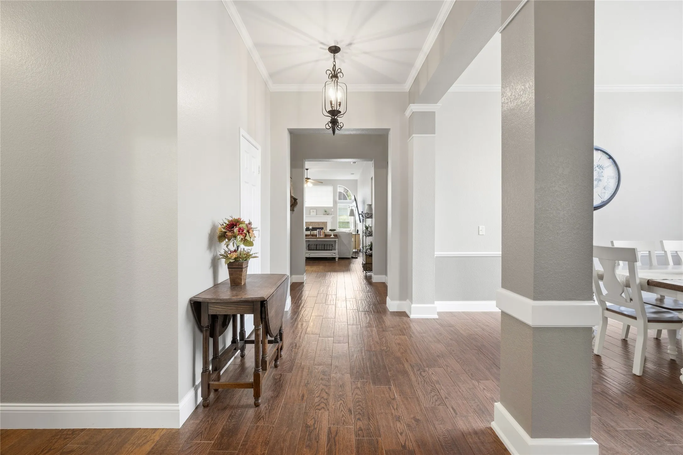 Hallway featuring wood-finish flooring, light gray walls, crown molding, and a decorative ceiling light fixture