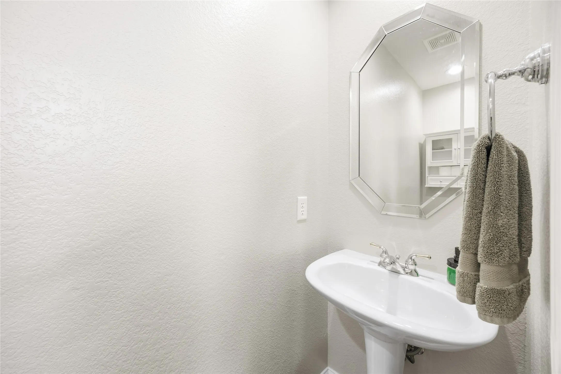 White pedestal sink with chrome faucet, octagonal framed mirror, and chrome towel bar