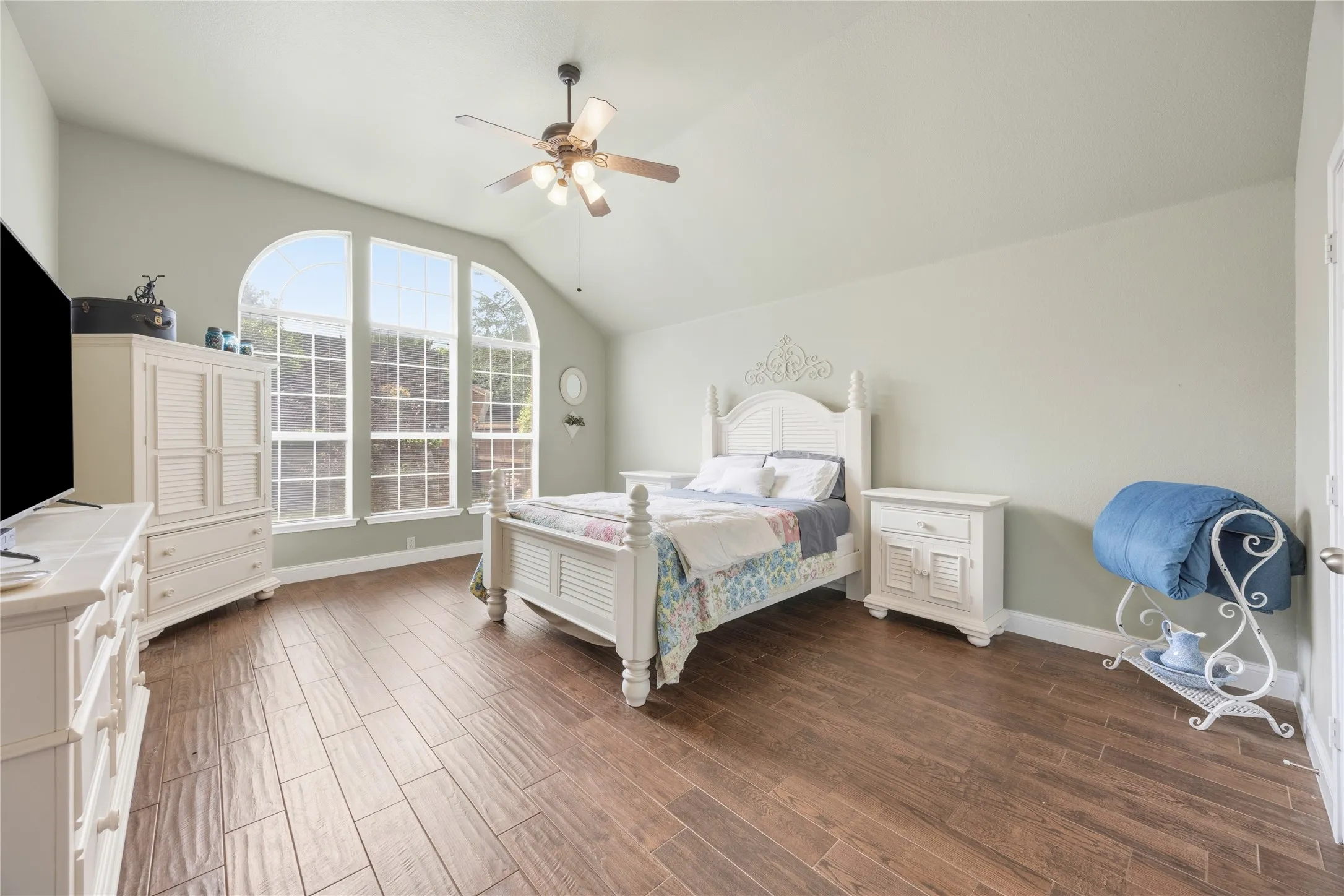 Vaulted ceiling with a ceiling fan, three arched windows, wood-finish flooring, and light-toned walls