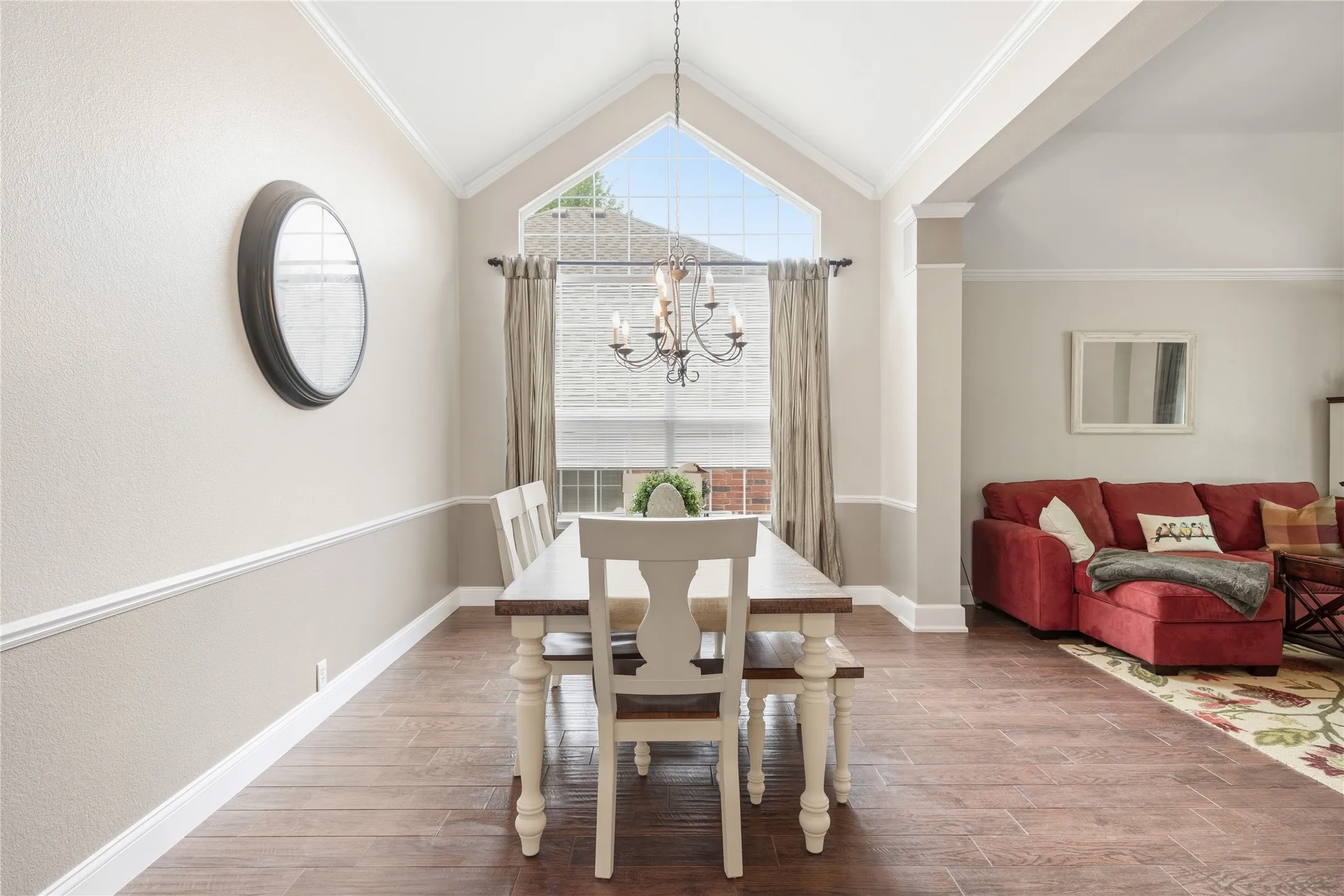 Vaulted ceiling dining area featuring wood-finish flooring, a decorative chandelier, and a large arched window with transom detailing